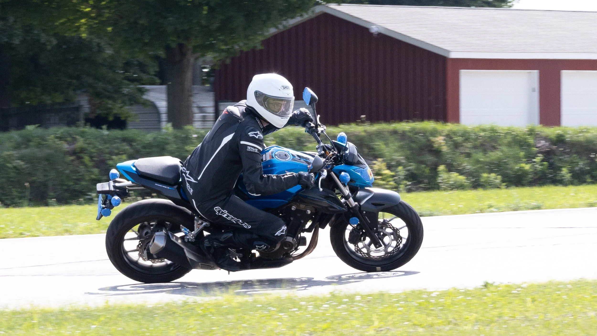 A motorcyclist wearing a white helmet and black riding gear riding a blue motorcycle on a suburban street.