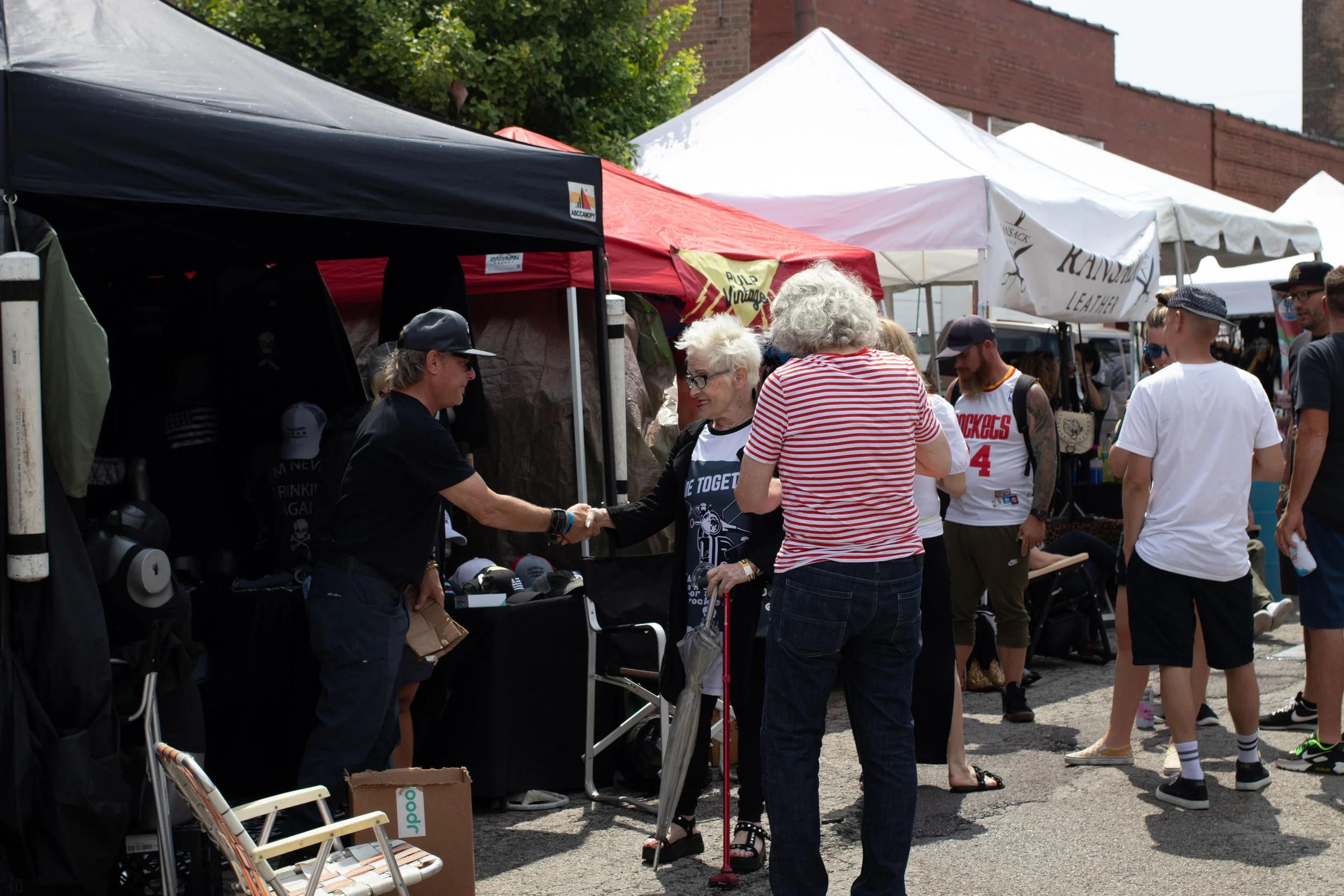 People at an outdoor market with tents, shopping, and socializing during daytime.