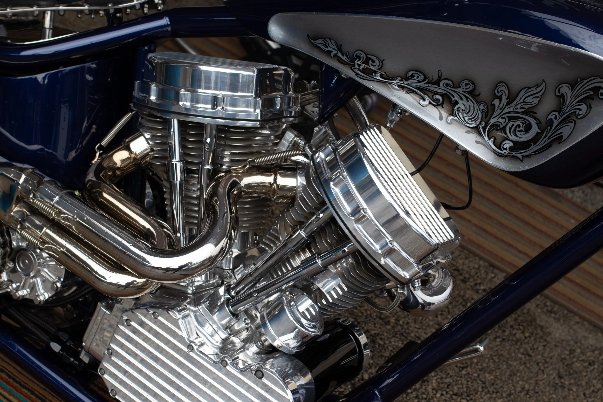 Close-up of a shiny, chrome motorcycle engine with intricate black and gray decorative artwork on the fuel tank.