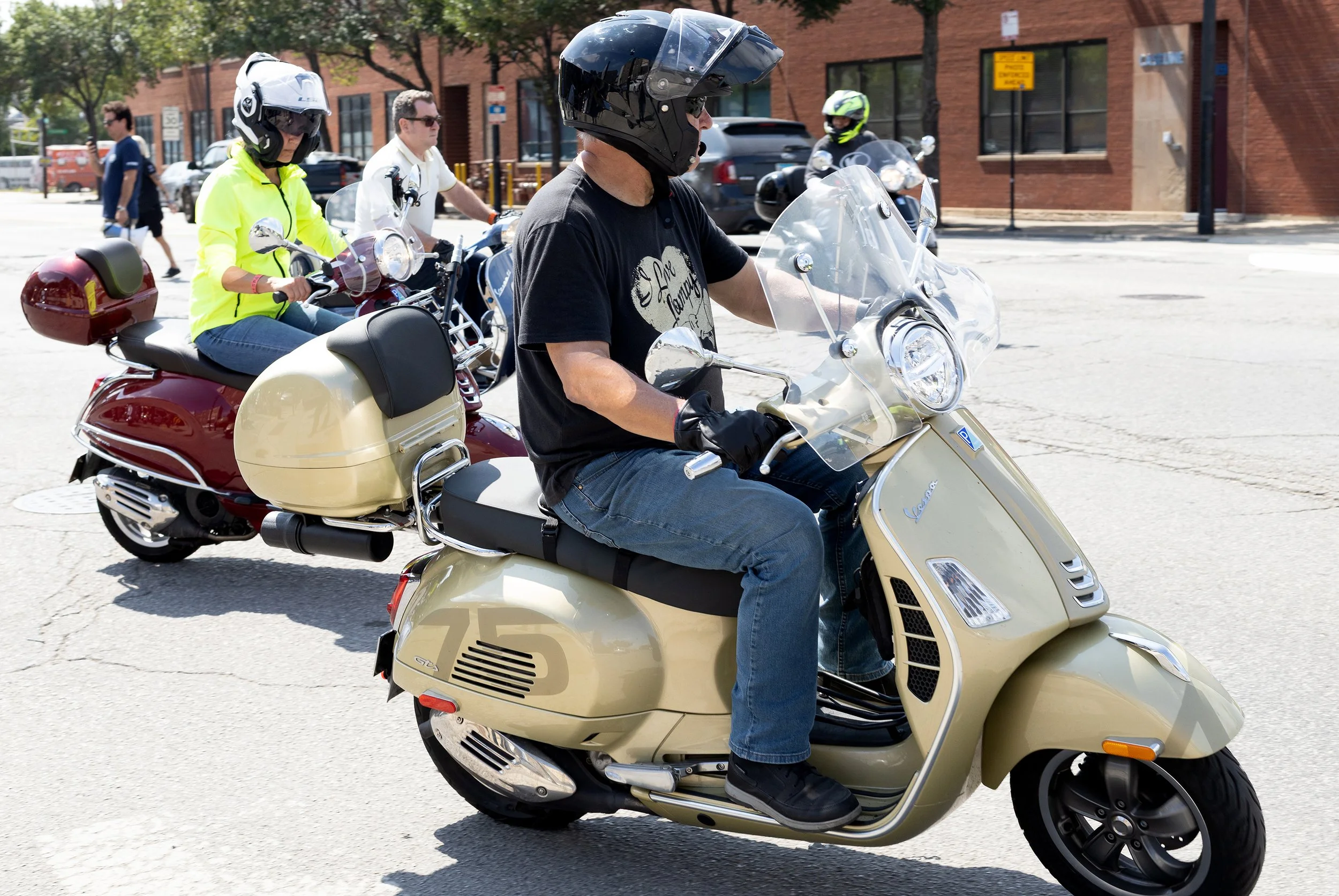 People riding scooters on a city street, all wearing helmets.