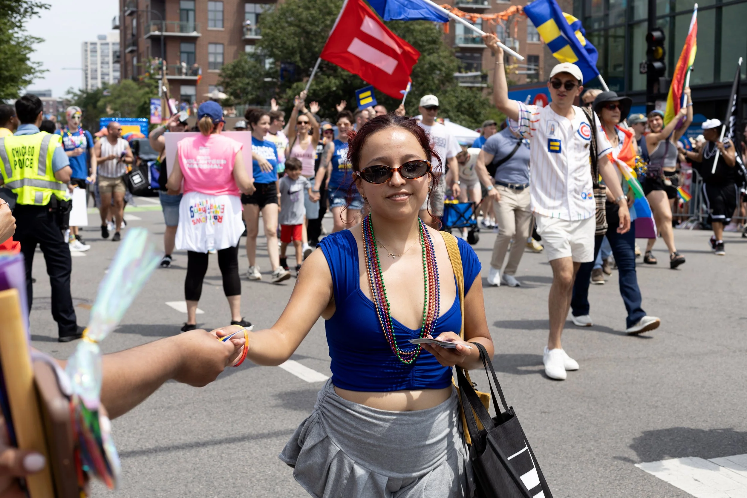 A group of people participating in a pride parade or celebration on the street, with some holding flags, wearing colorful clothing and accessories.