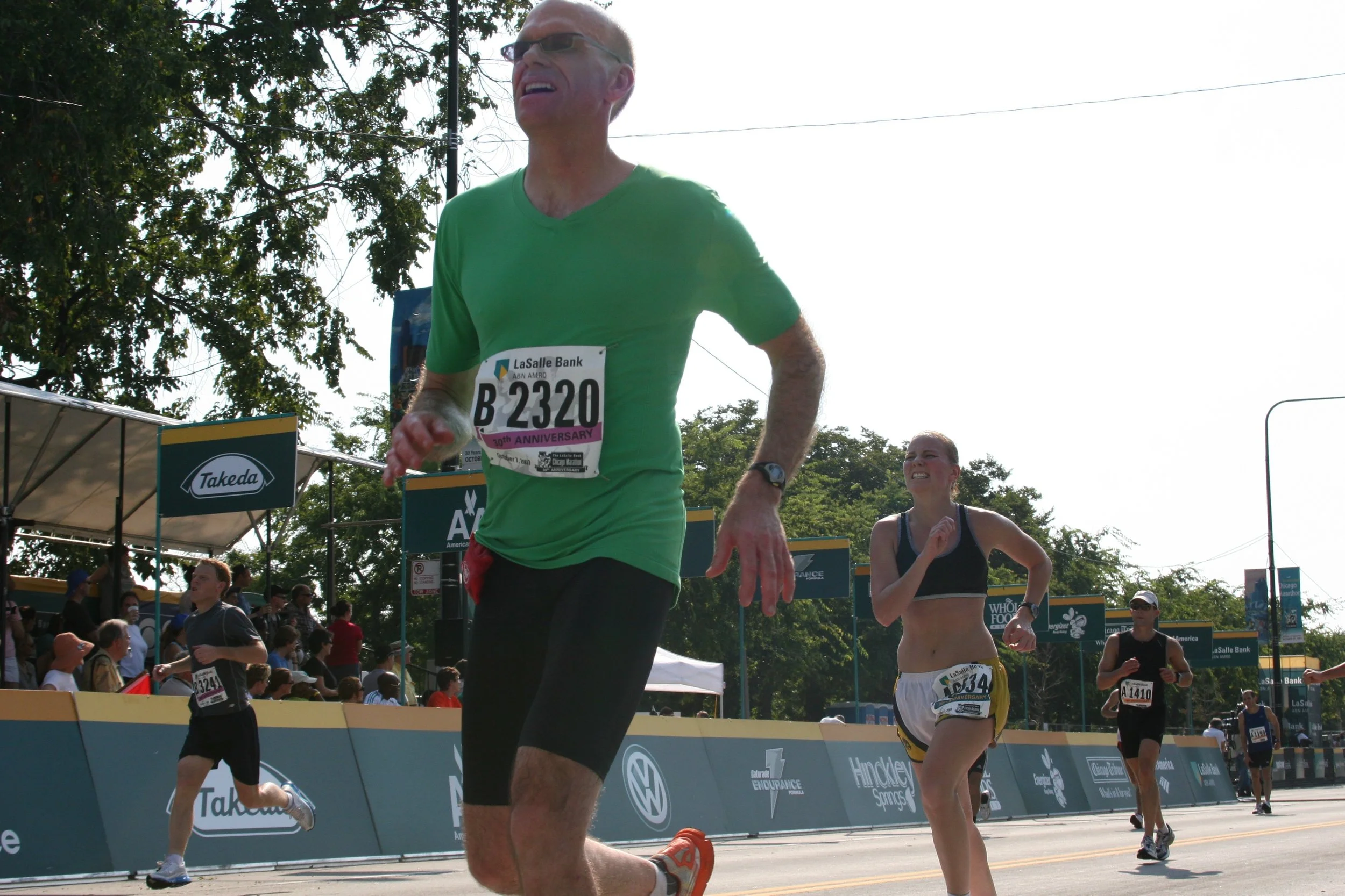 Runners competing in a marathon race on a sunny day, with race banners and spectators in the background.