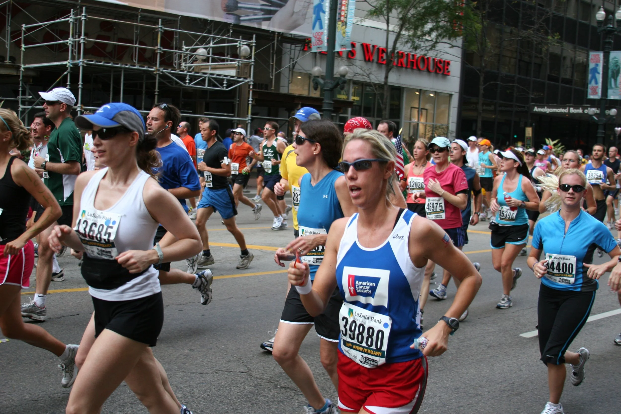 A large group of marathon runners participating in a race on a city street with buildings and banners in the background.