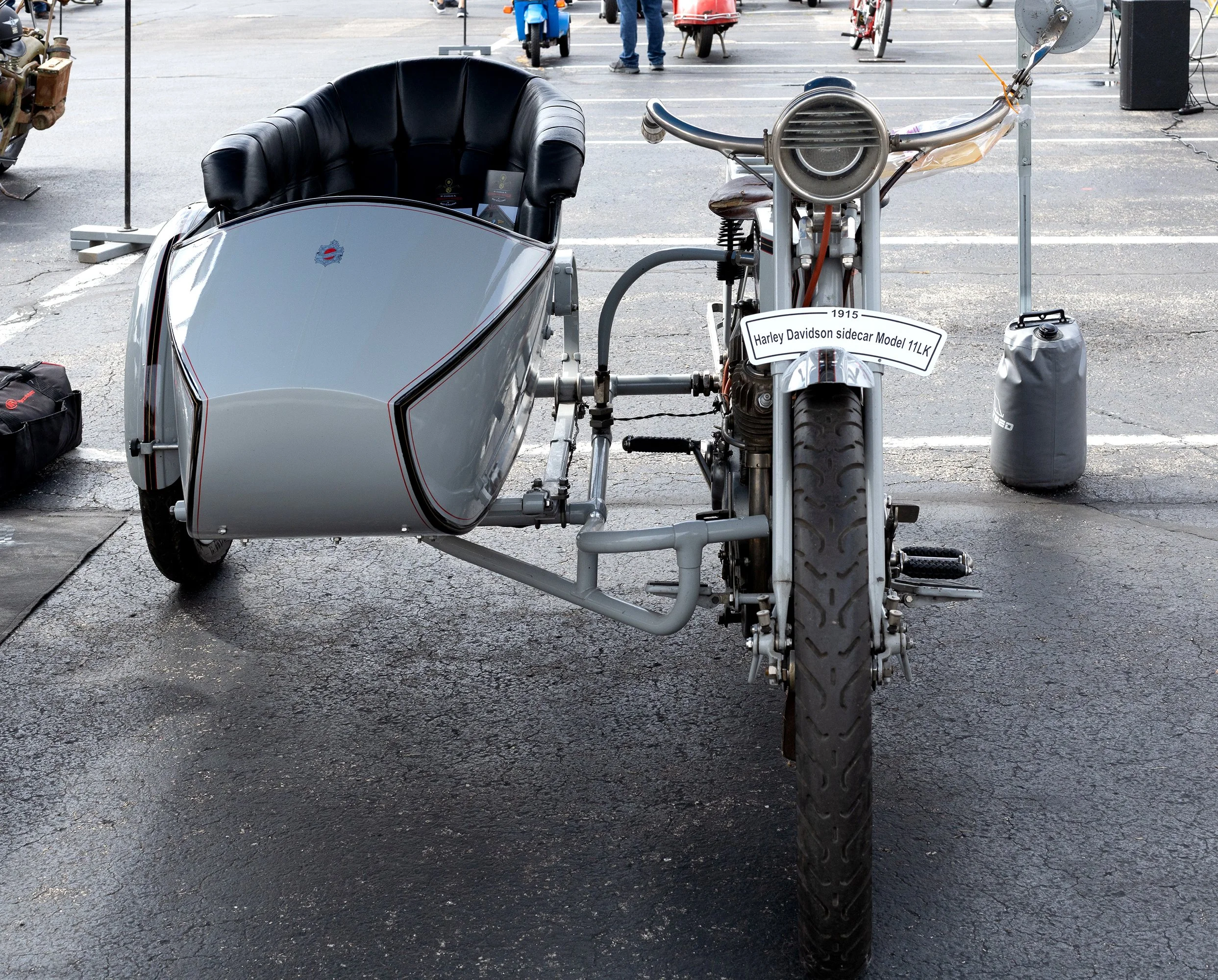 A motorized Harley Davidson sidecar motorcycle Model 11LK parked in a lot with other motorcycles and scooters in the background.