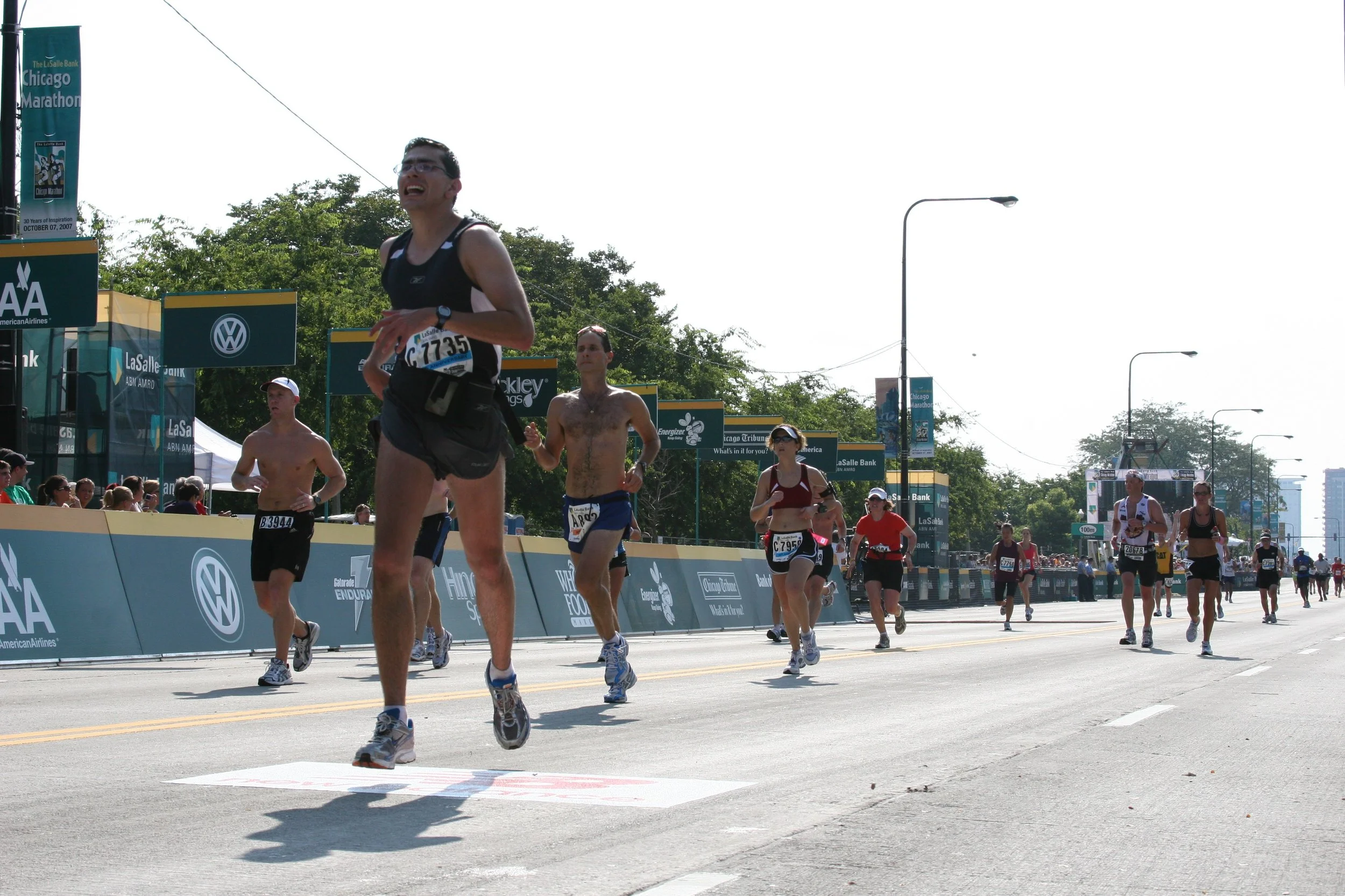 A group of marathon runners participating in the Chicago Marathon, running on a city street with race banners and spectators watching.