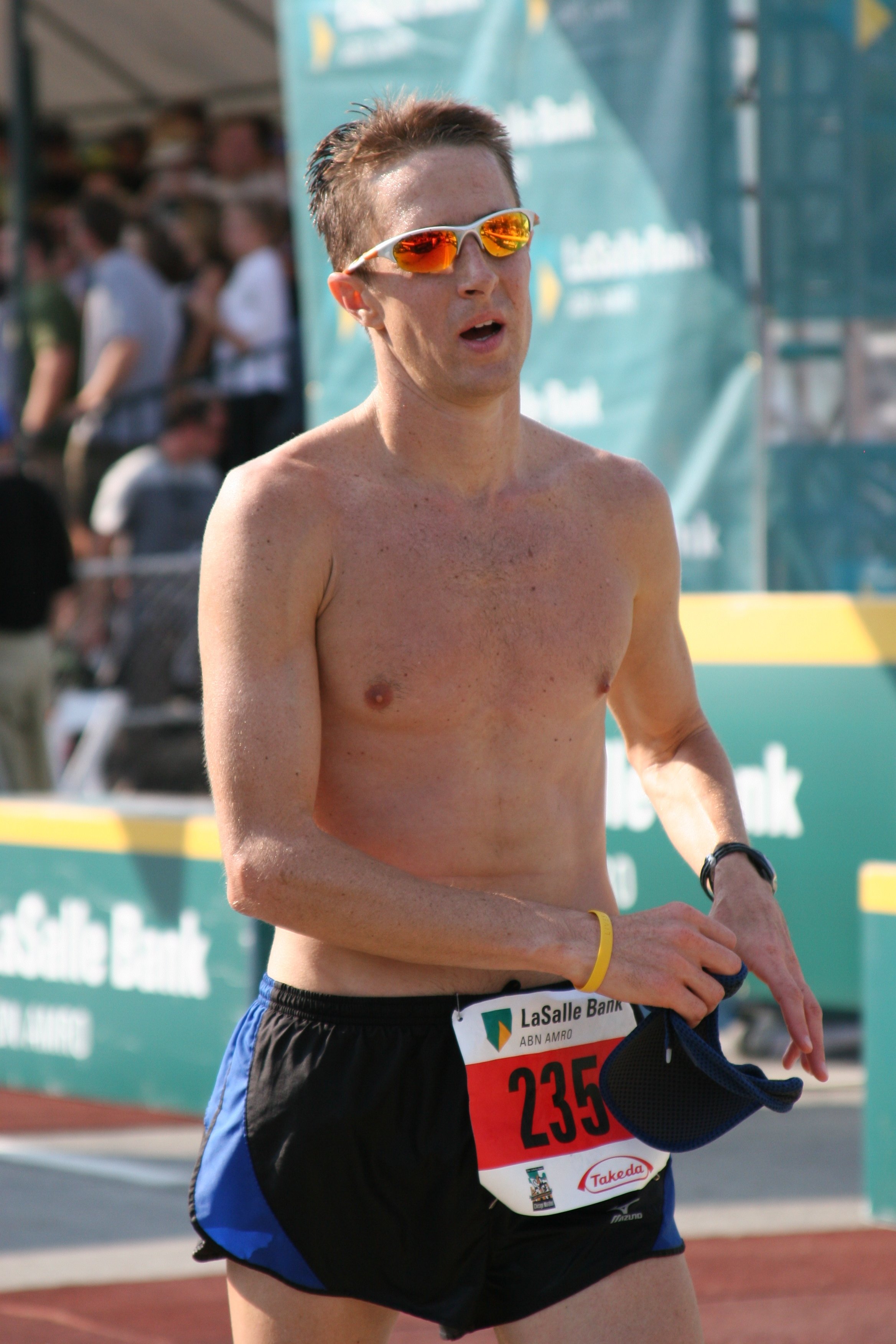A male marathon runner with sunglasses and a race bib running outdoors during a race event.