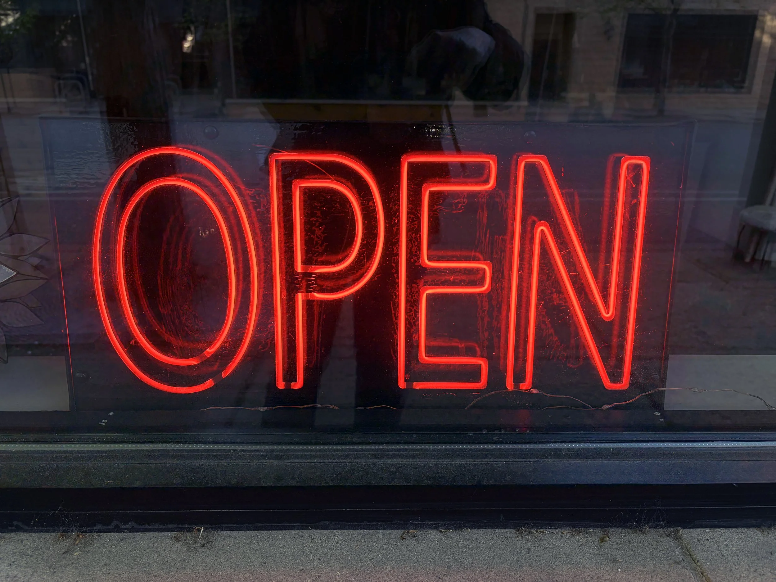 A red neon sign displaying the word 'OPEN' placed behind a glass window.