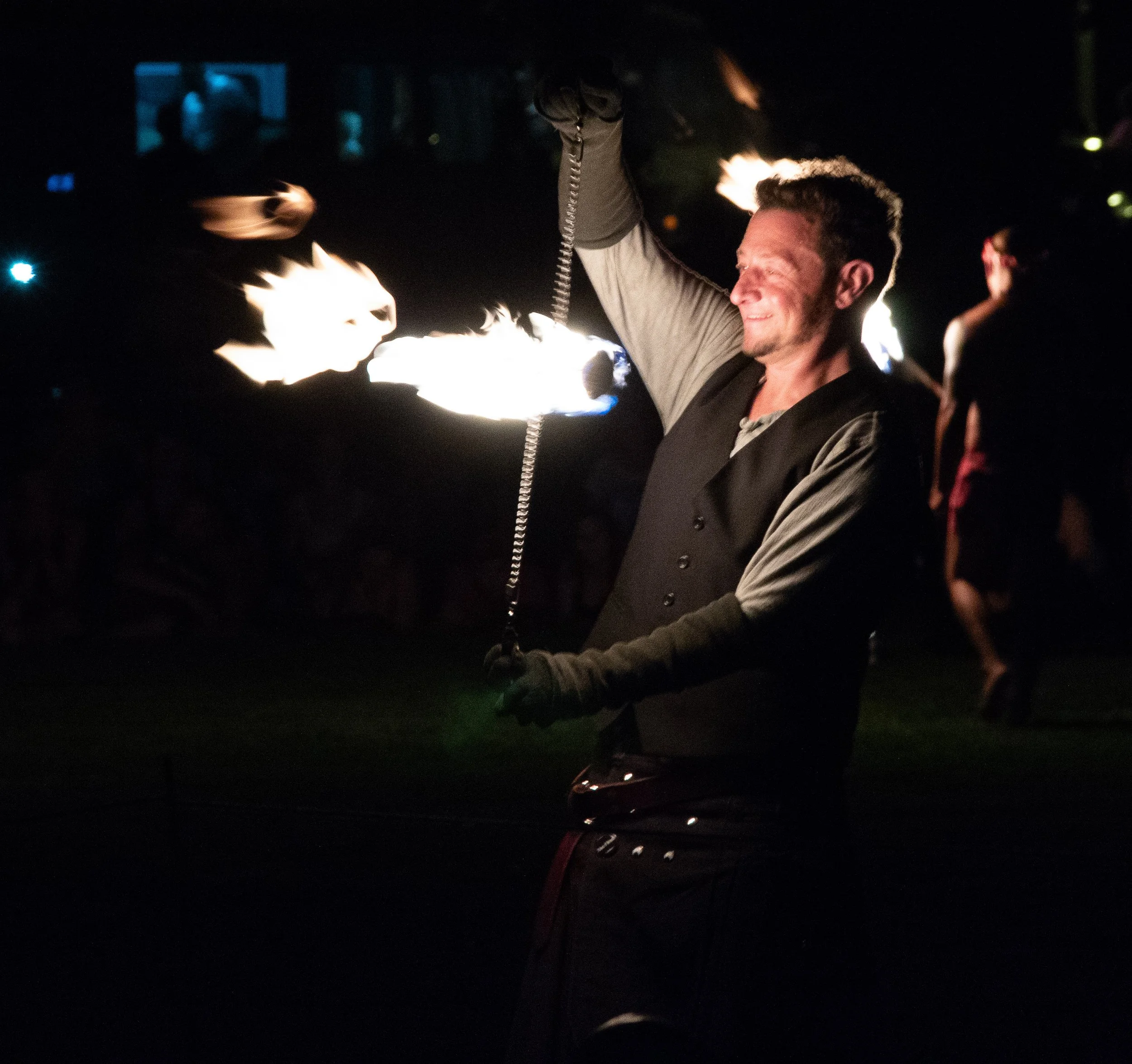 A man smiling at night while holding a flaming torch with fire reflecting on his face.