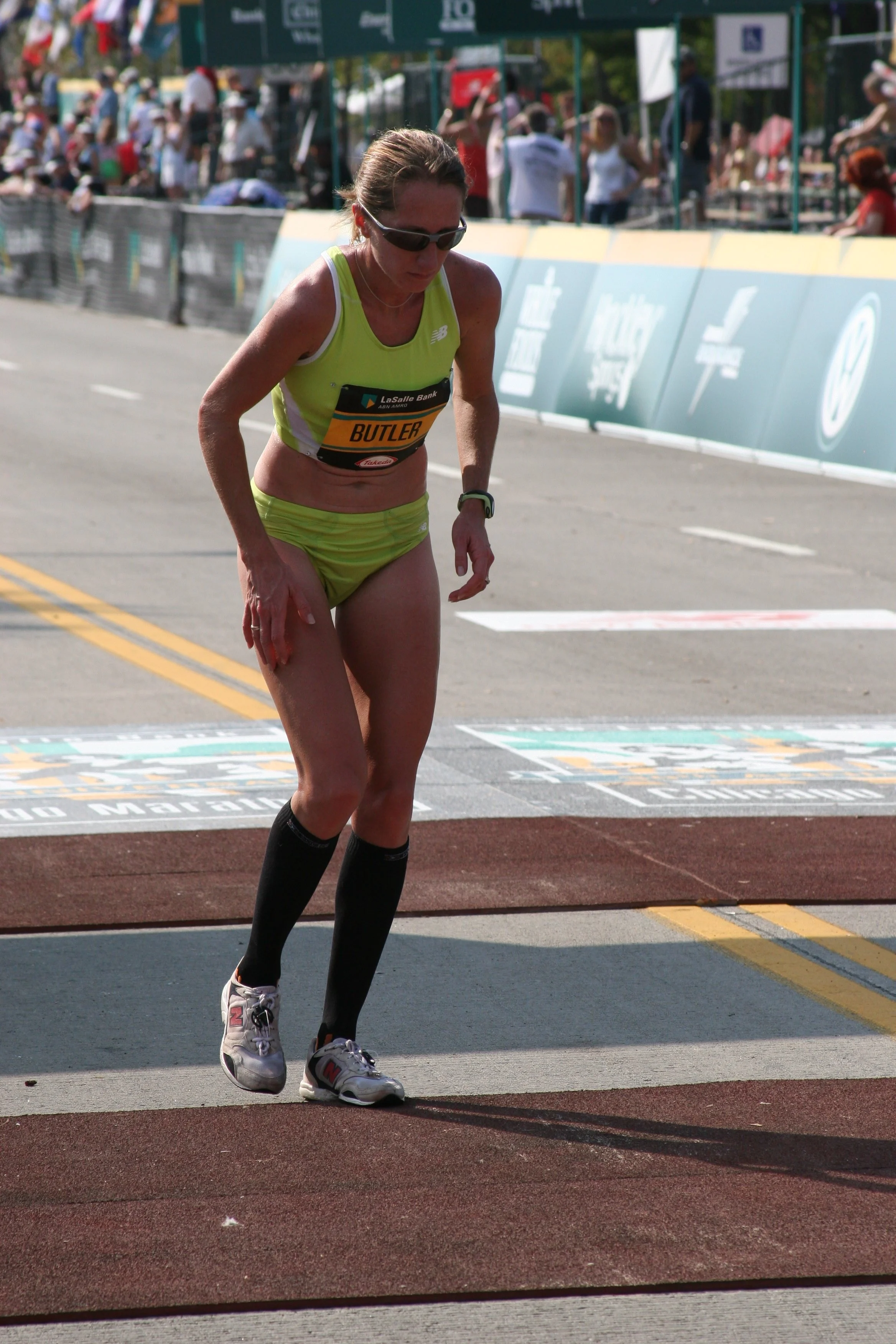 Female athlete in bright yellow sportswear running in a marathon, crossing the finish line, with a crowd of spectators in the background.