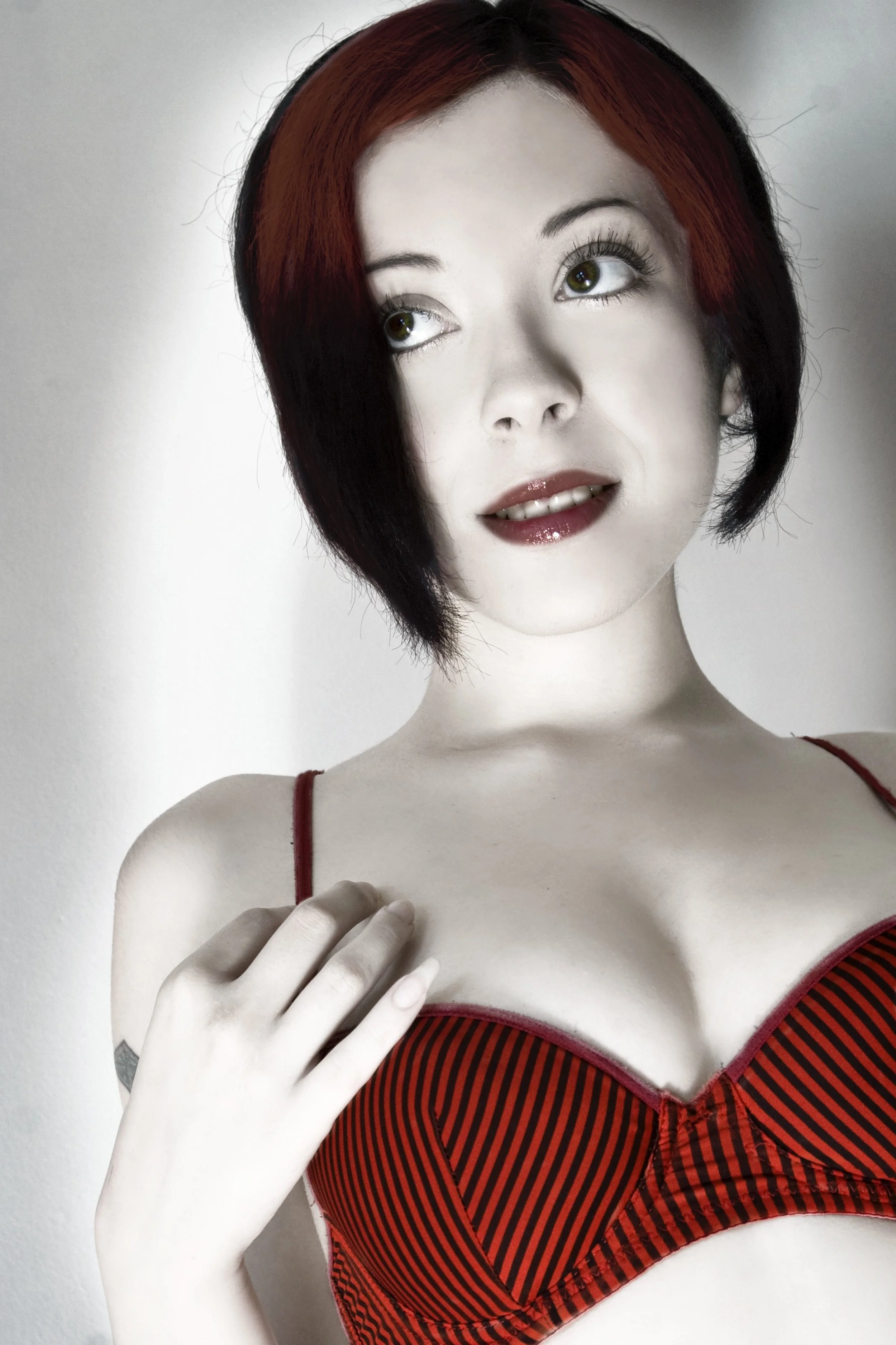 A mannequin with short dark red hair and green eyes, wearing a red and black striped bra, holding a hand near its chest, positioned against a neutral background.