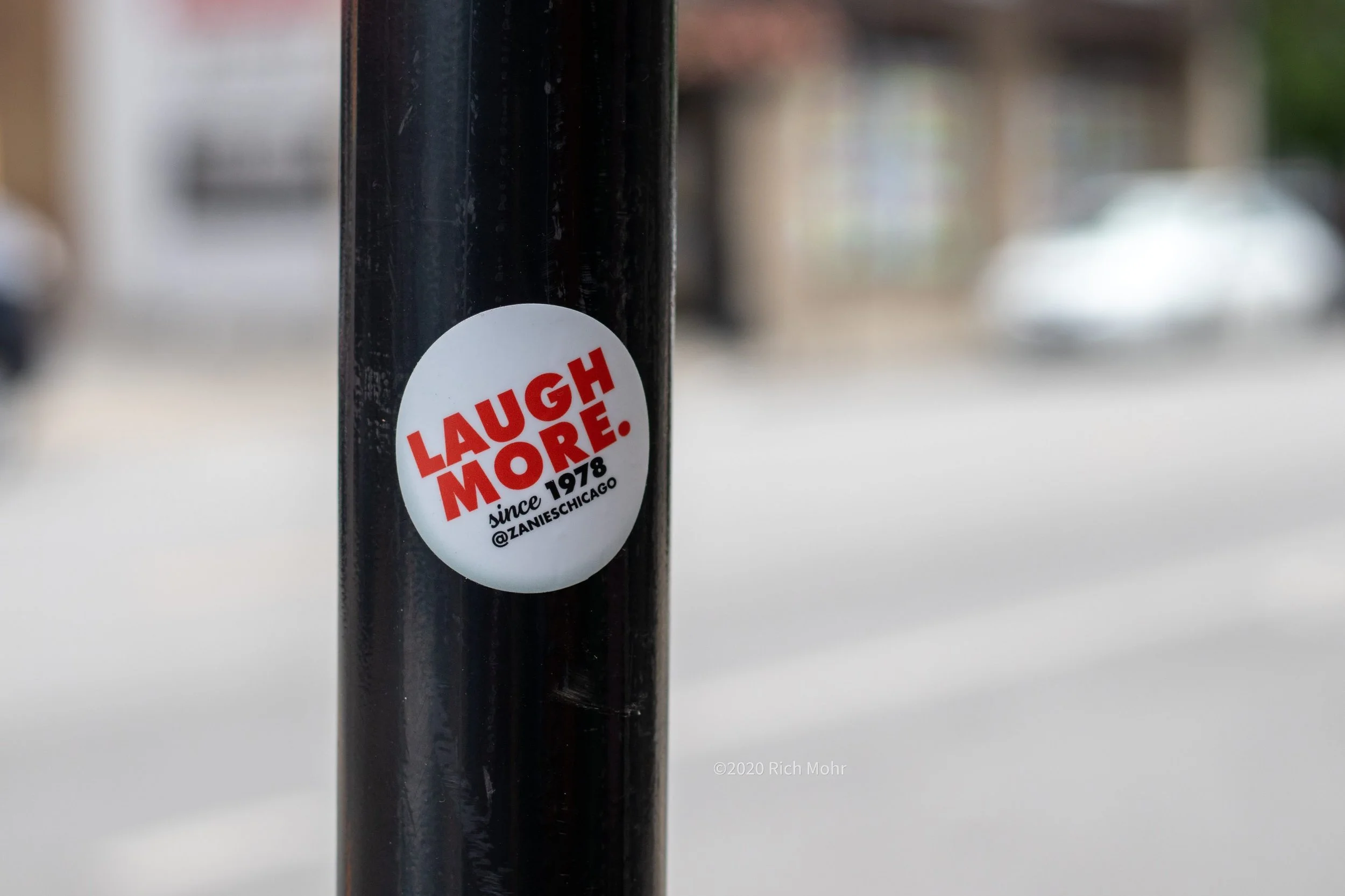 A sticker on a black pole reads 'LAUGH MORE. since 1978 @ZANIESCHICAGO' with a blurred background.