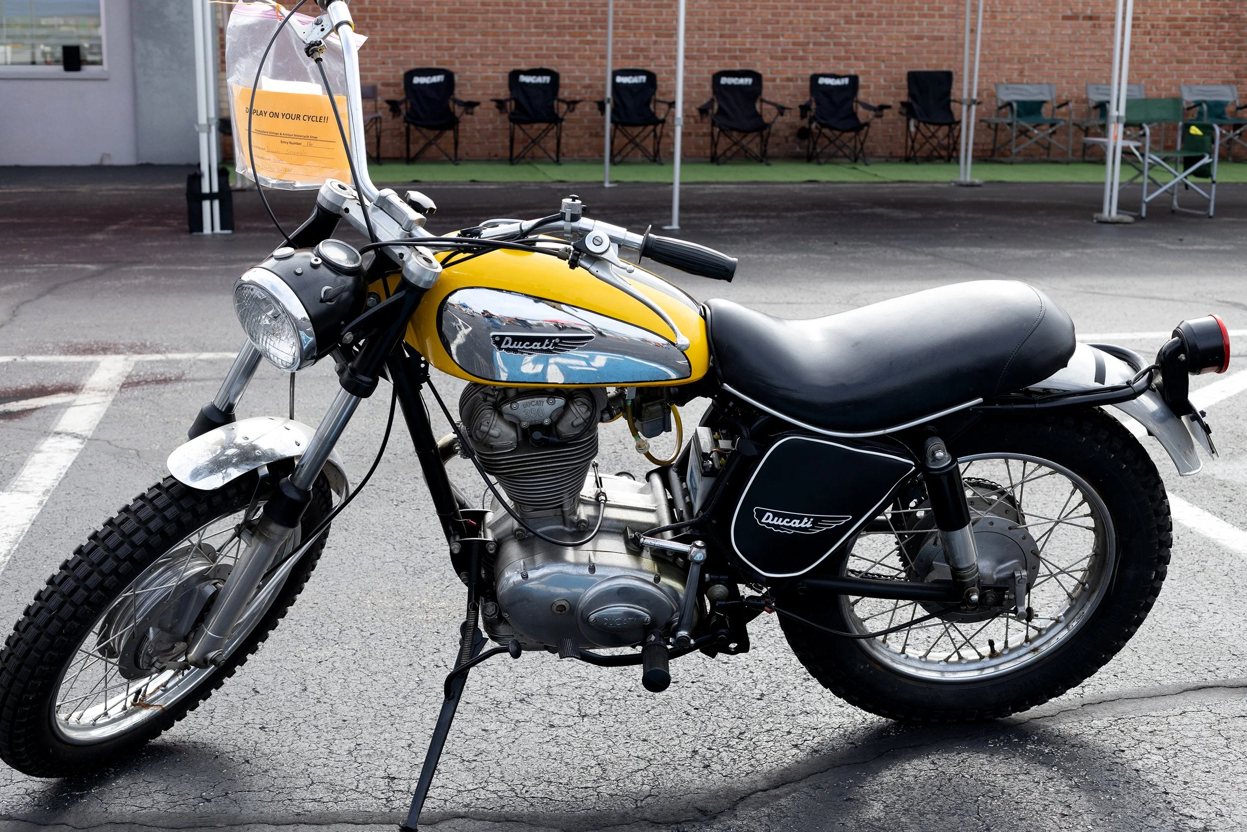 A yellow and black Ducati motorcycle parked on a pavement with chairs and tents in the background.