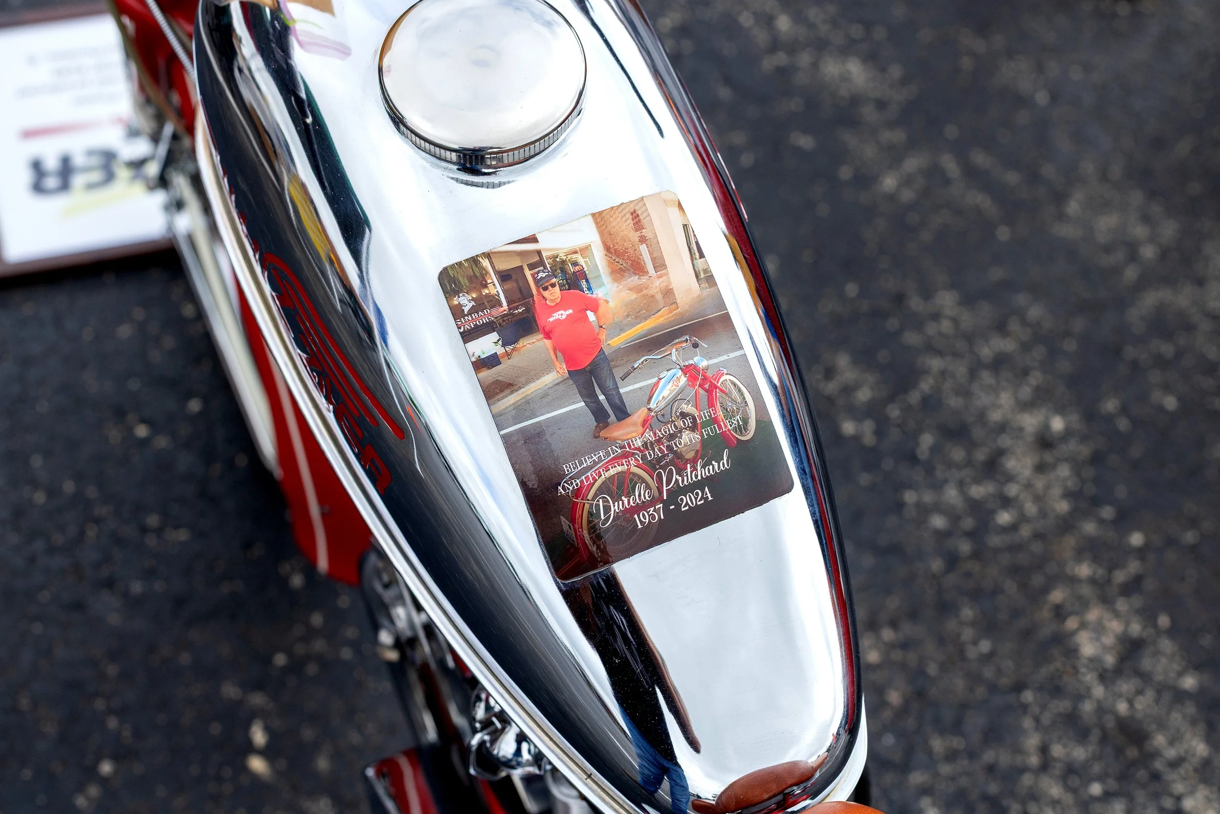 A shiny metal object with a sticker of a woman standing next to a bicycle, and a text that reads 'Believe in the magic of life, and let every day to its fullest. Durello Prichard 1937-2024.'