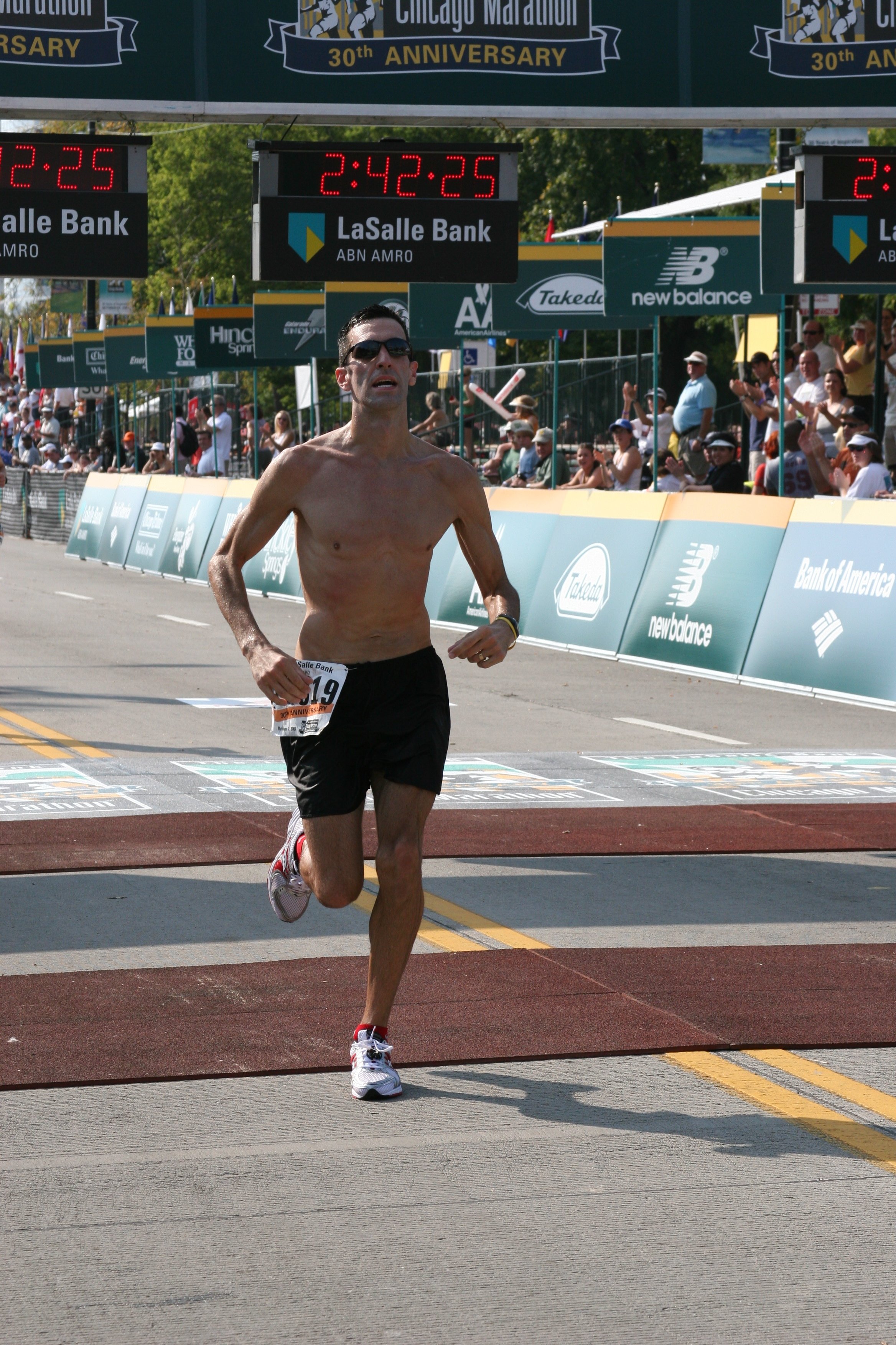A male runner shoes a determined expression as he crosses the finish line at a marathon event, surrounded by spectators and race signage.
