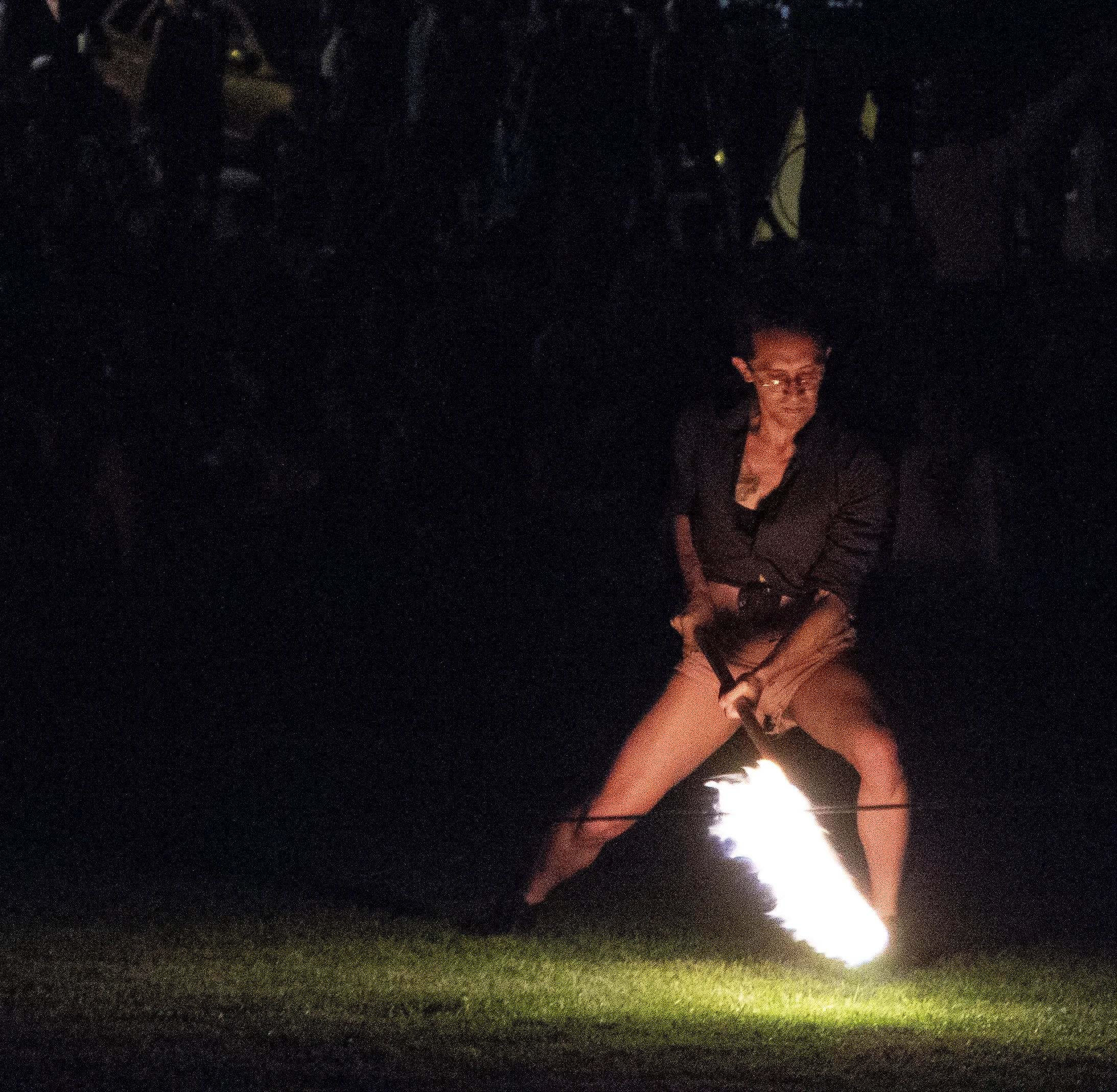 A person holding a lit flare or firework at night, with a dark background and faintly visible grass or ground.