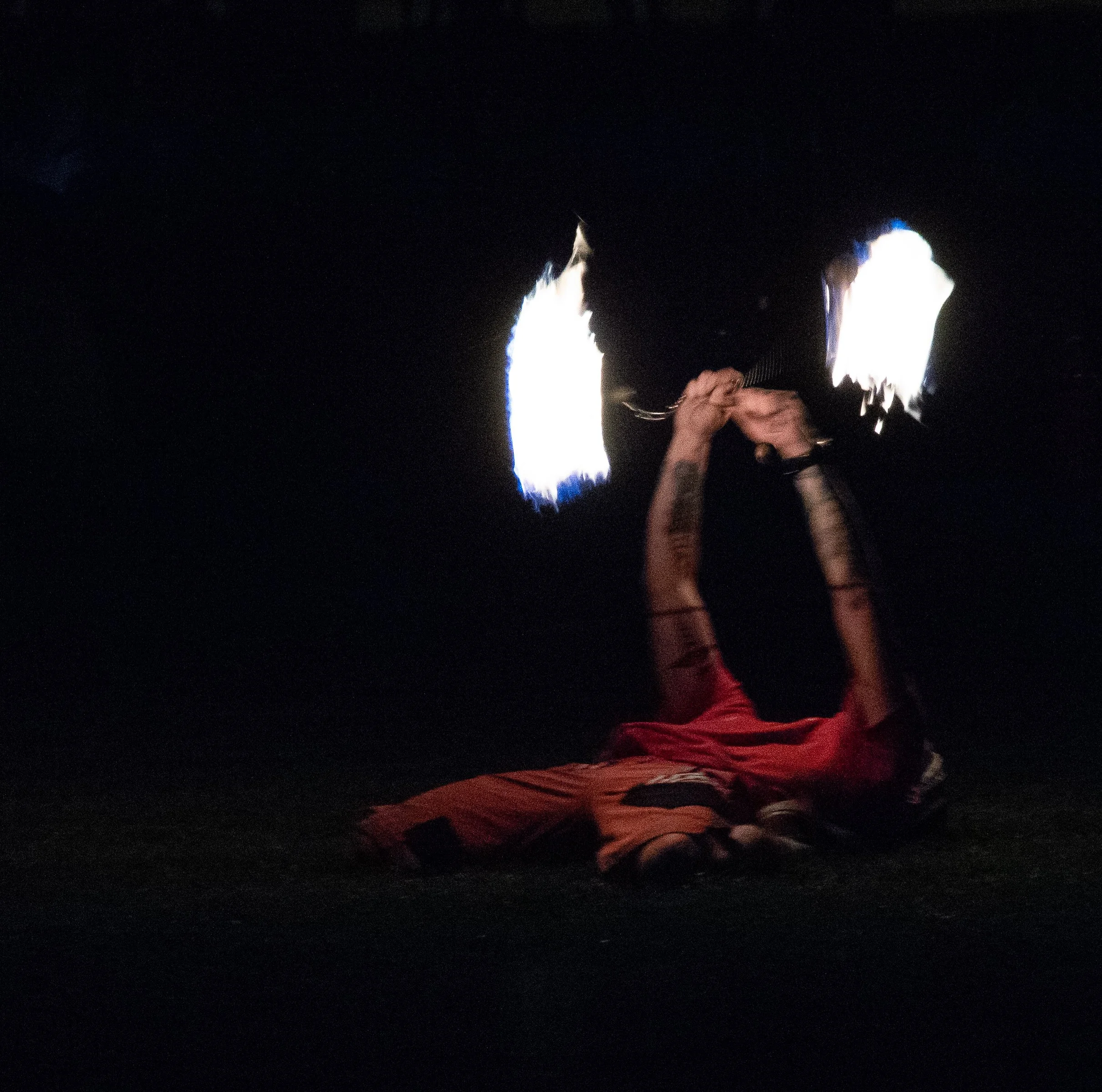 A person performing a fire-breathing stunt at night with flames arcing outward.