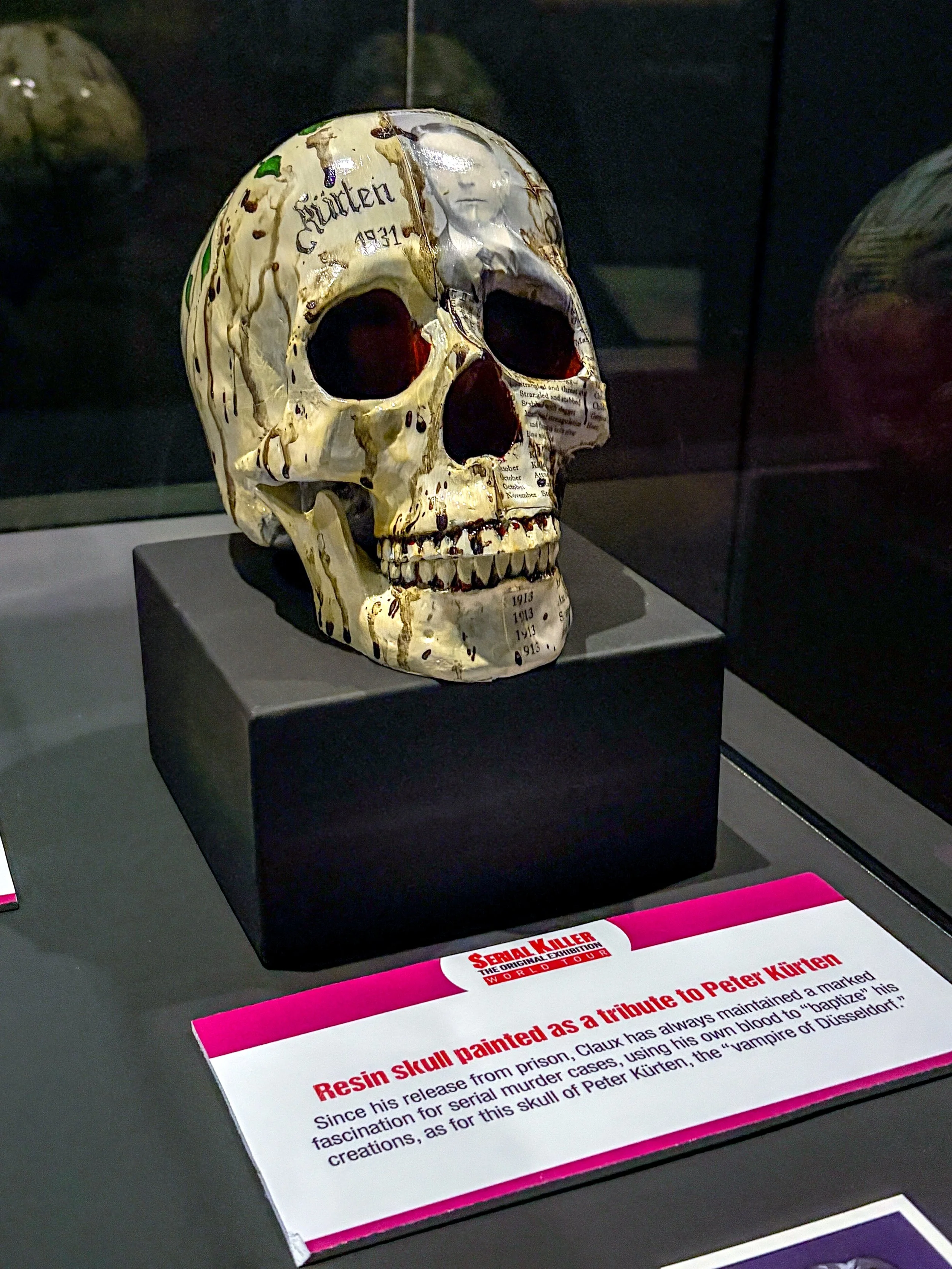 Resin skull painted as a tribute to Peter Kürten, displayed on a black pedestal with an informational placard below.