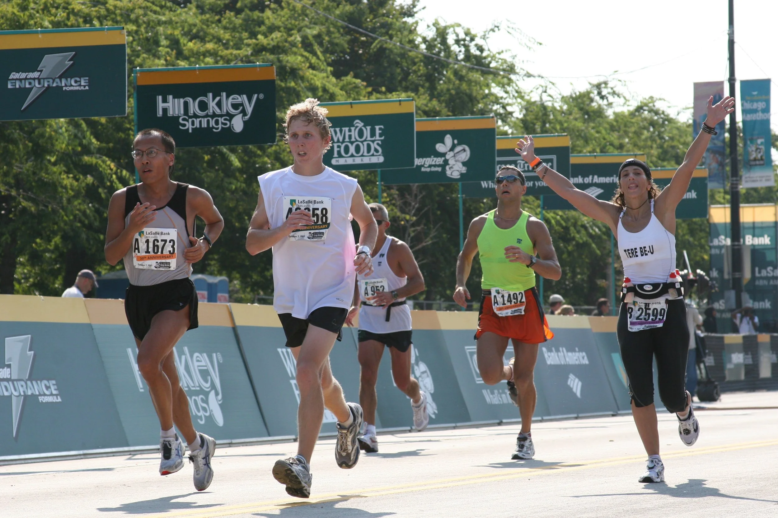 Group of marathon runners crossing the finish line during a race, with trees and banners in the background.