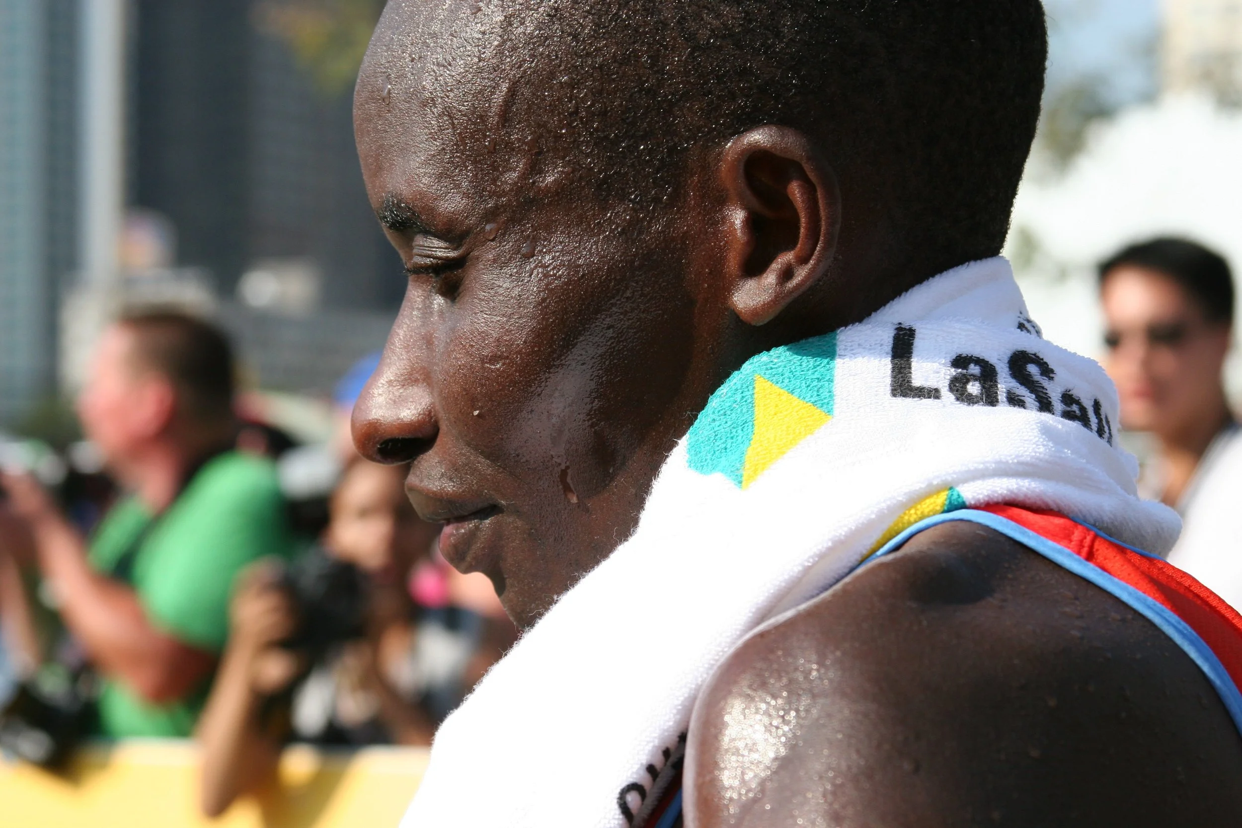 Close-up of a male athlete with sweat on his face, wearing a white towel with a colorful pattern around his neck, after a sports event.
