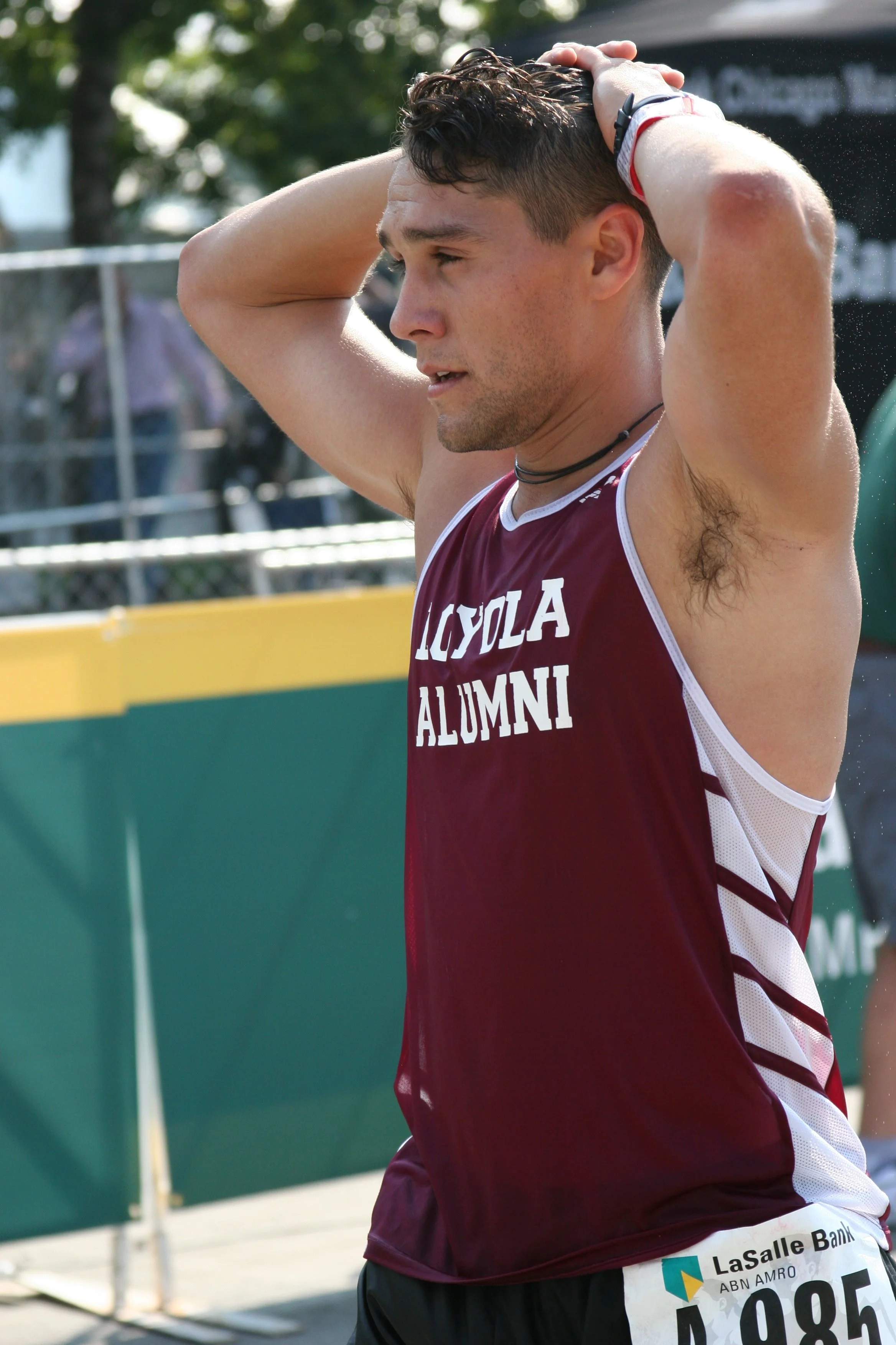 A male athlete with a bib number 085, wearing a maroon and white jersey that reads 'LOYOLA A...' and text 'LaSalle Bank' on his shorts, is standing outdoors with his hands on his head after a race.