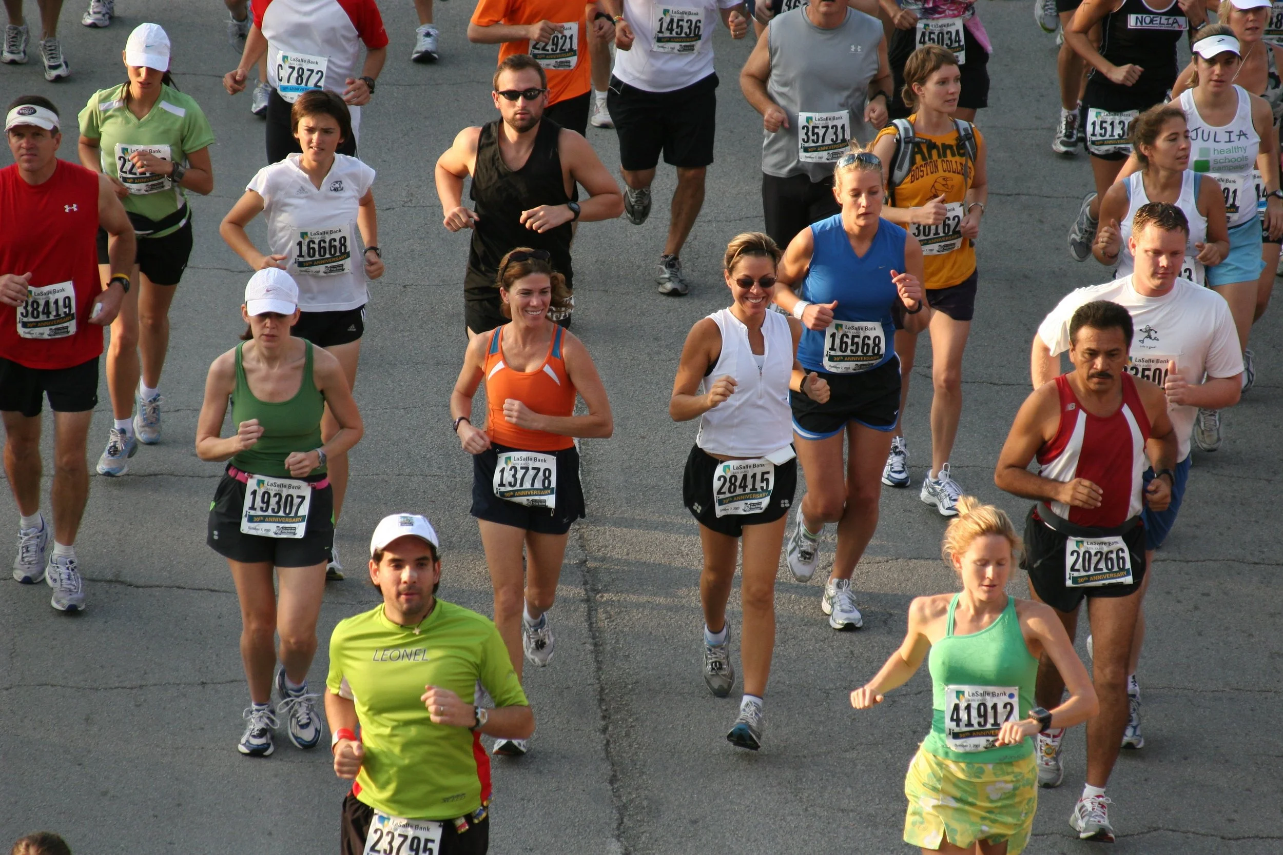 A group of people participating in a marathon race, running on a paved road wearing athletic clothes and race bibs.