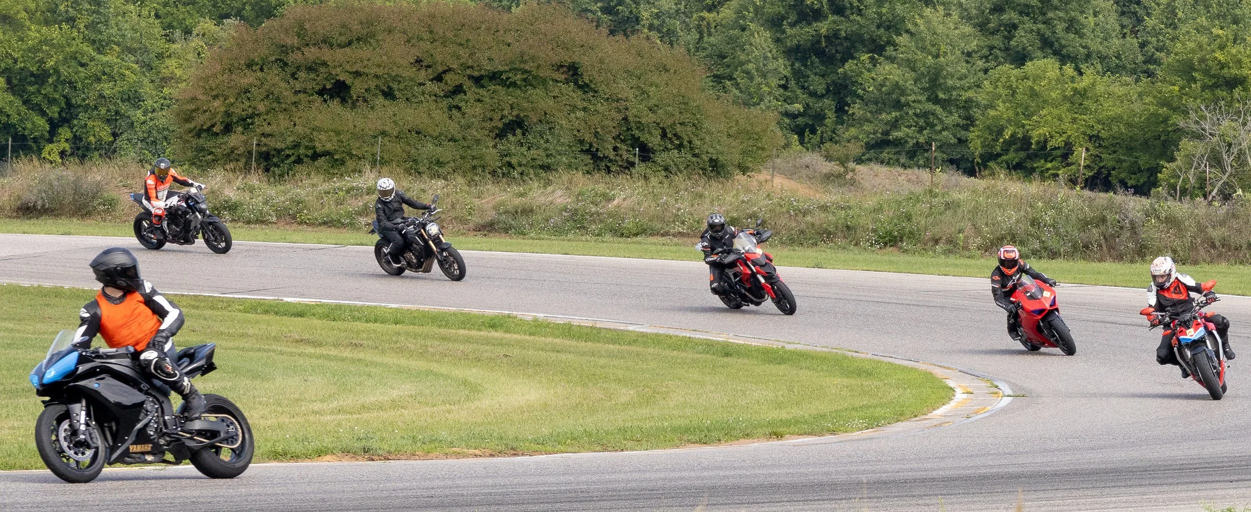Six motorcyclists riding on a curving road surrounded by greenery.