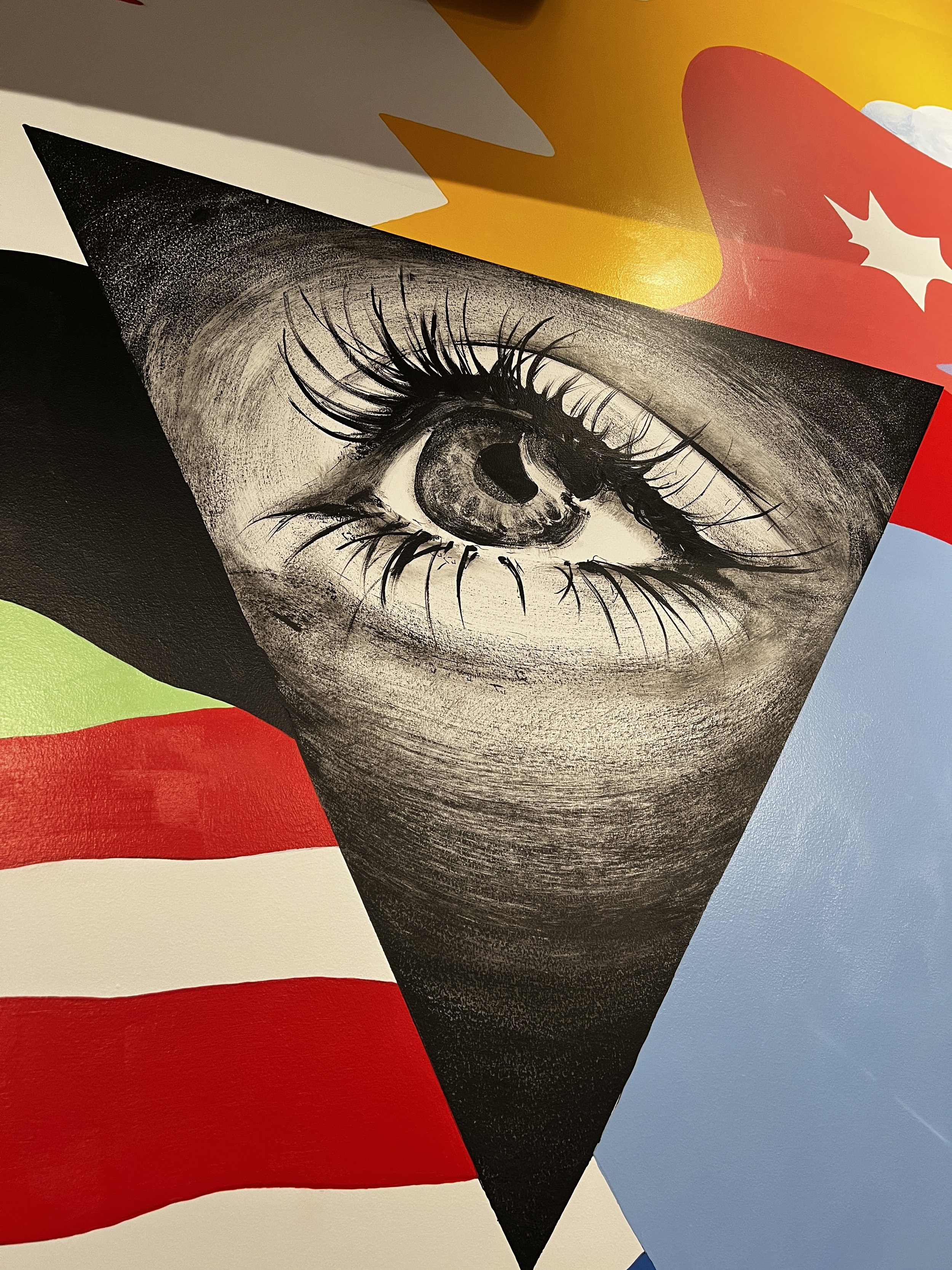 Close-up of a black and white drawing of a human eye on paper, with parts of the American flag in the background.