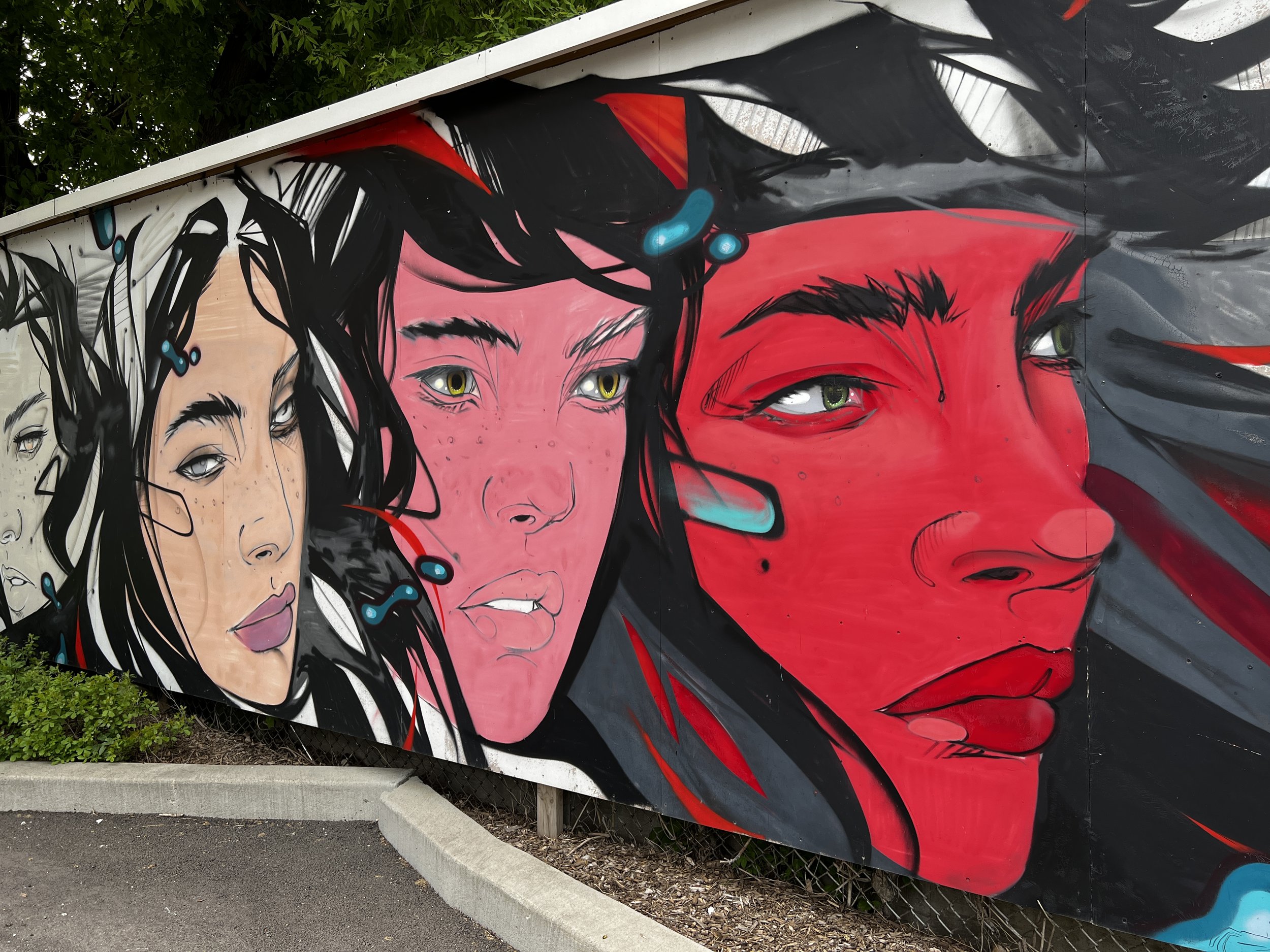 Colorful mural of three women with distinct facial features and makeup, painted on an outdoor wall.