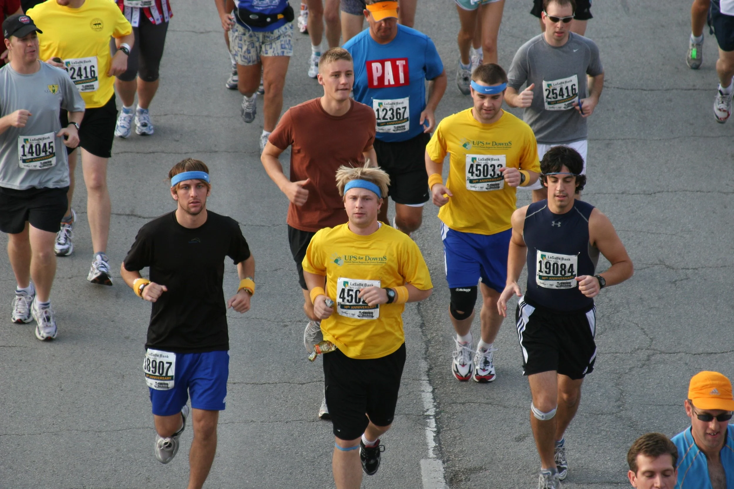 A group of marathon runners participating in a race, wearing race bibs and athletic clothing, running on a city street.