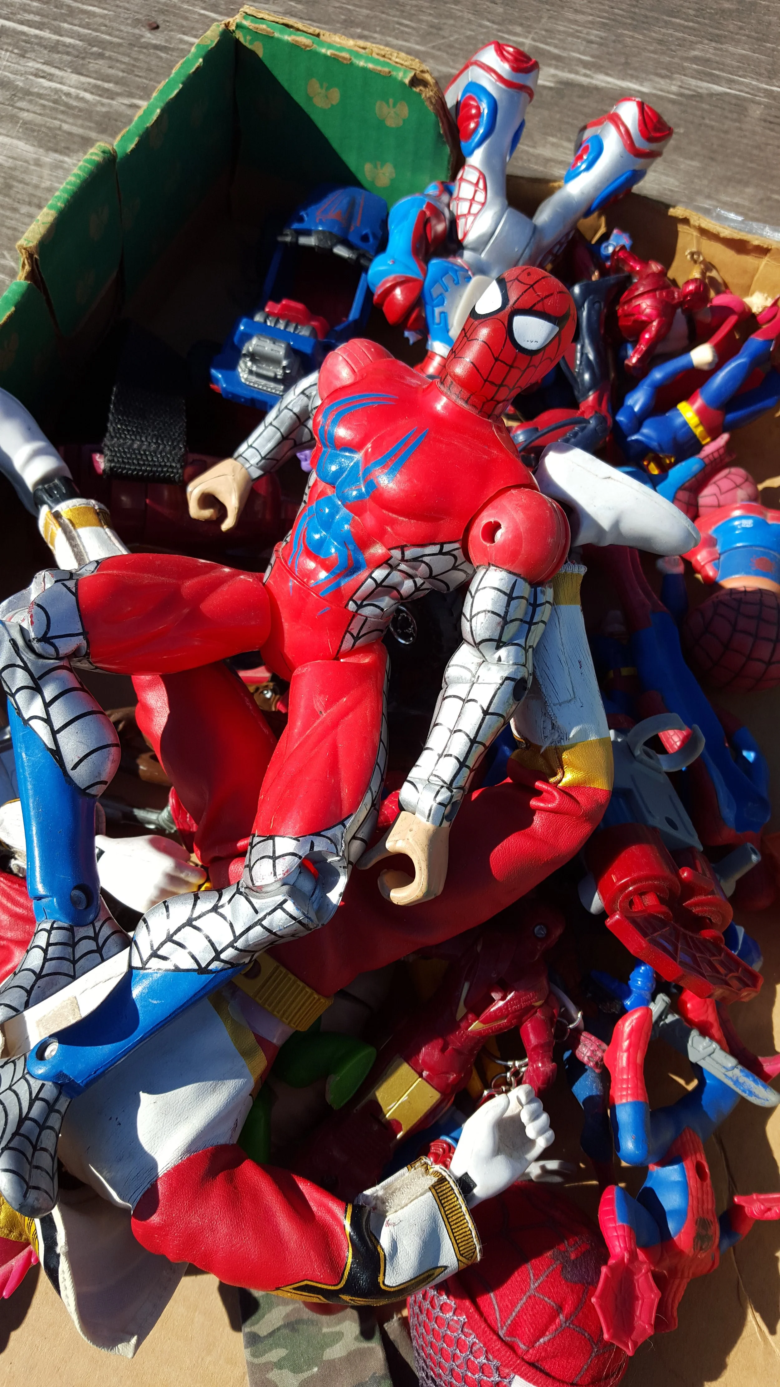 A pile of various superhero and action figure toys on a wooden surface, including Spider-Man, Iron Man, and other characters.