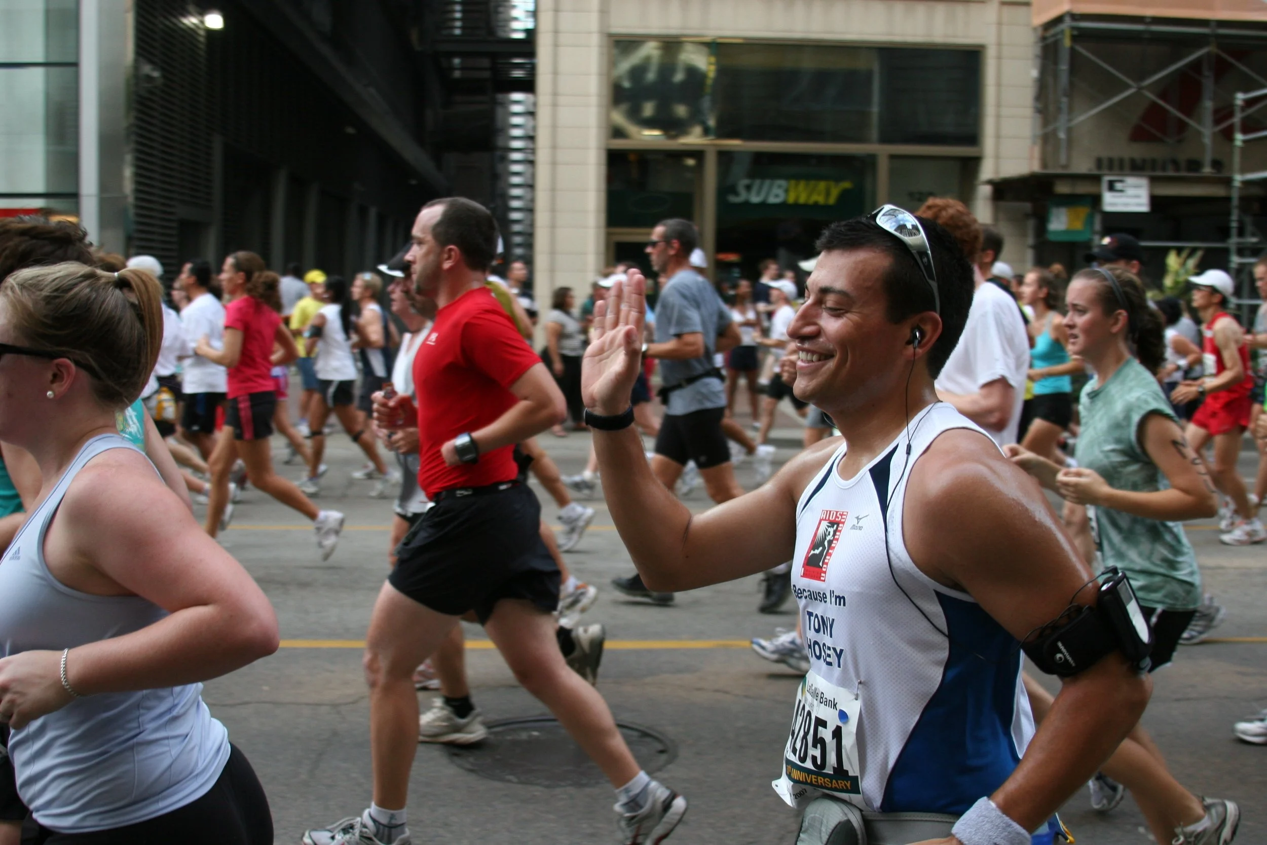 A group of marathon runners participating in a race on a city street, with a smiling male runner showing a high-five gesture.