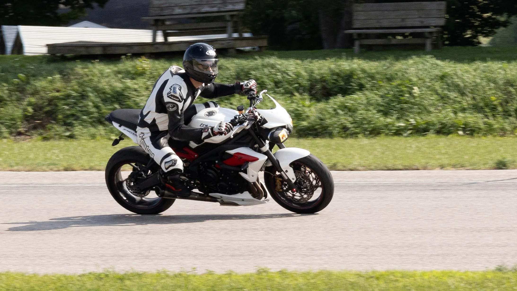 Motorcycle rider wearing a black helmet and riding a black and white motorcycle on a road with a grassy background.