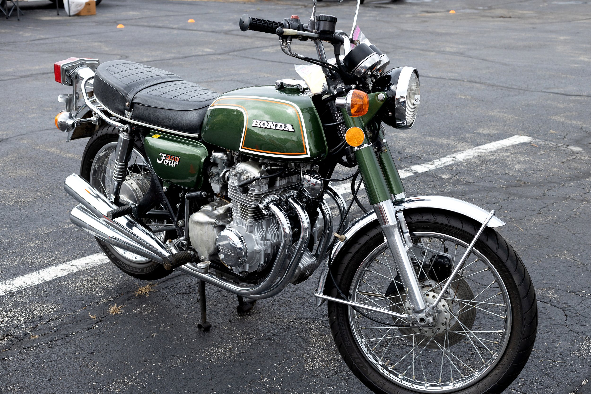 A vintage green Honda motorcycle parked in a parking lot with asphalt pavement.