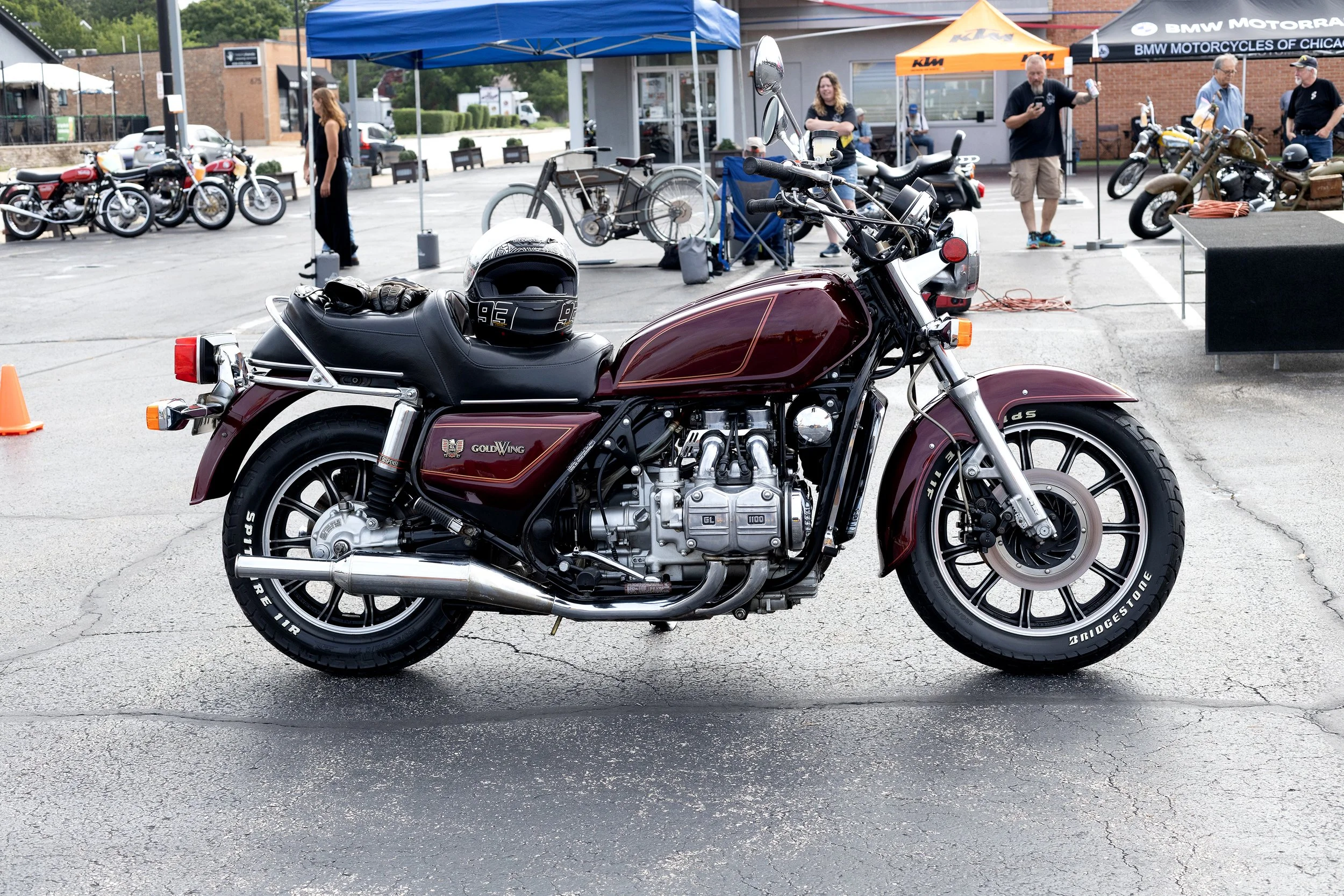 A maroon and black Harley Davidson motorcycle parked in a lot during a motorcycle event, with several other motorcycles and people in the background.