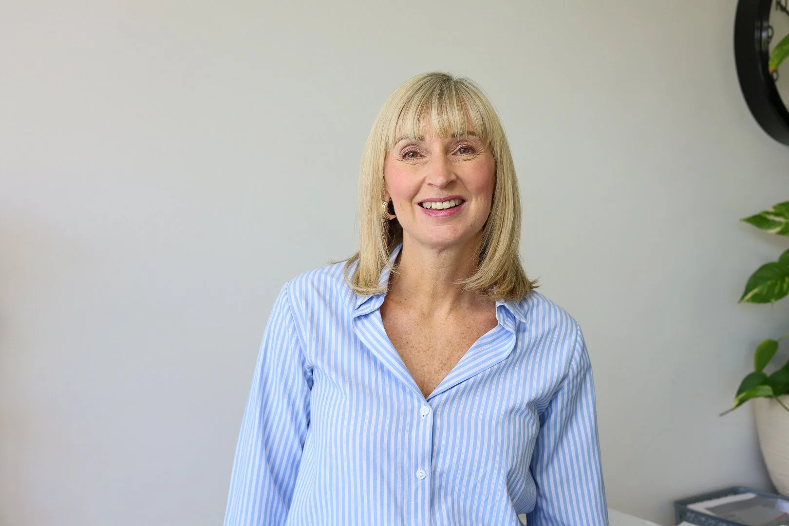 A woman with blonde hair, wearing a green blouse, smiling against a plain white background.