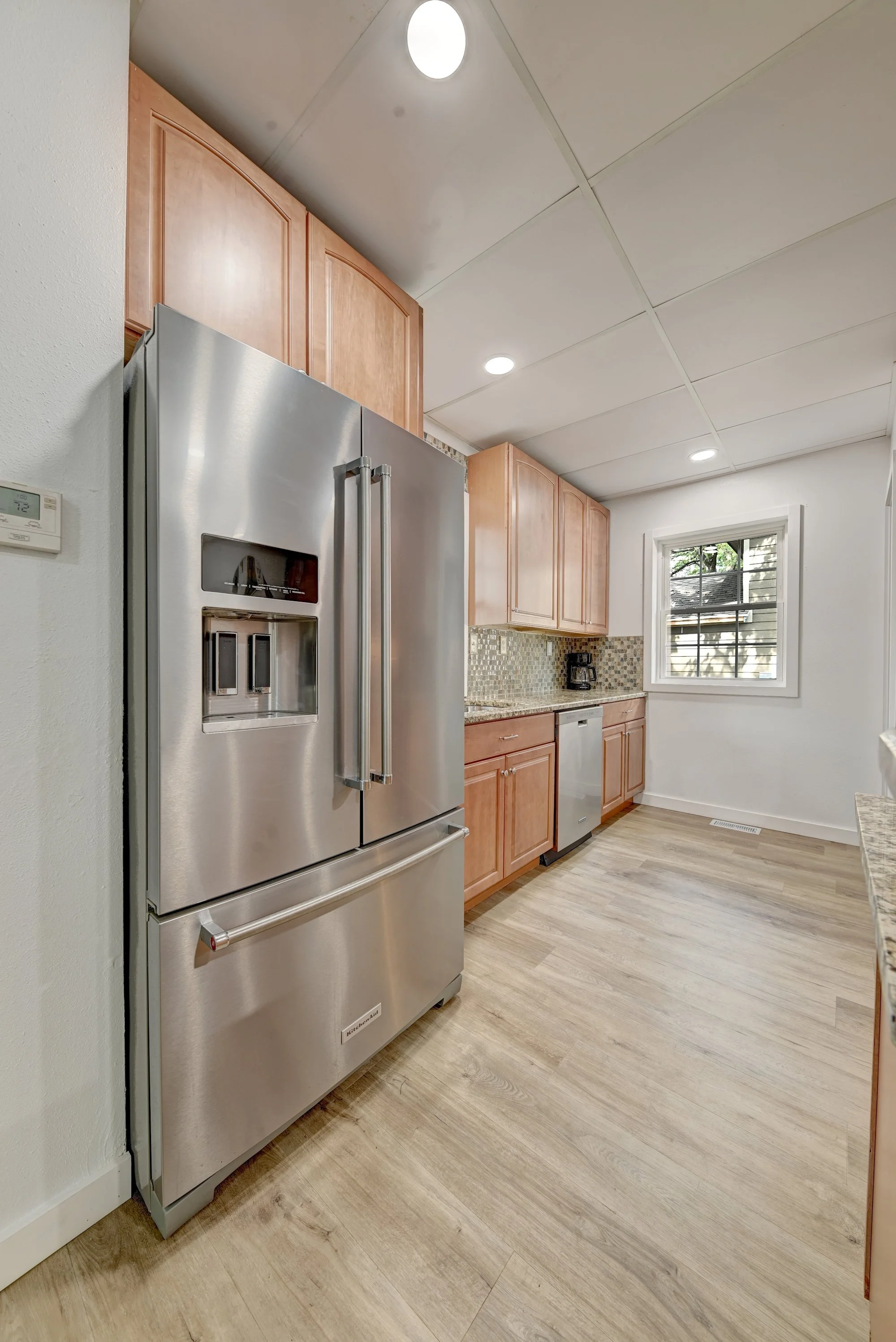Kitchen with a stainless steel refrigerator, wooden cabinets, a small window, and wooden flooring.