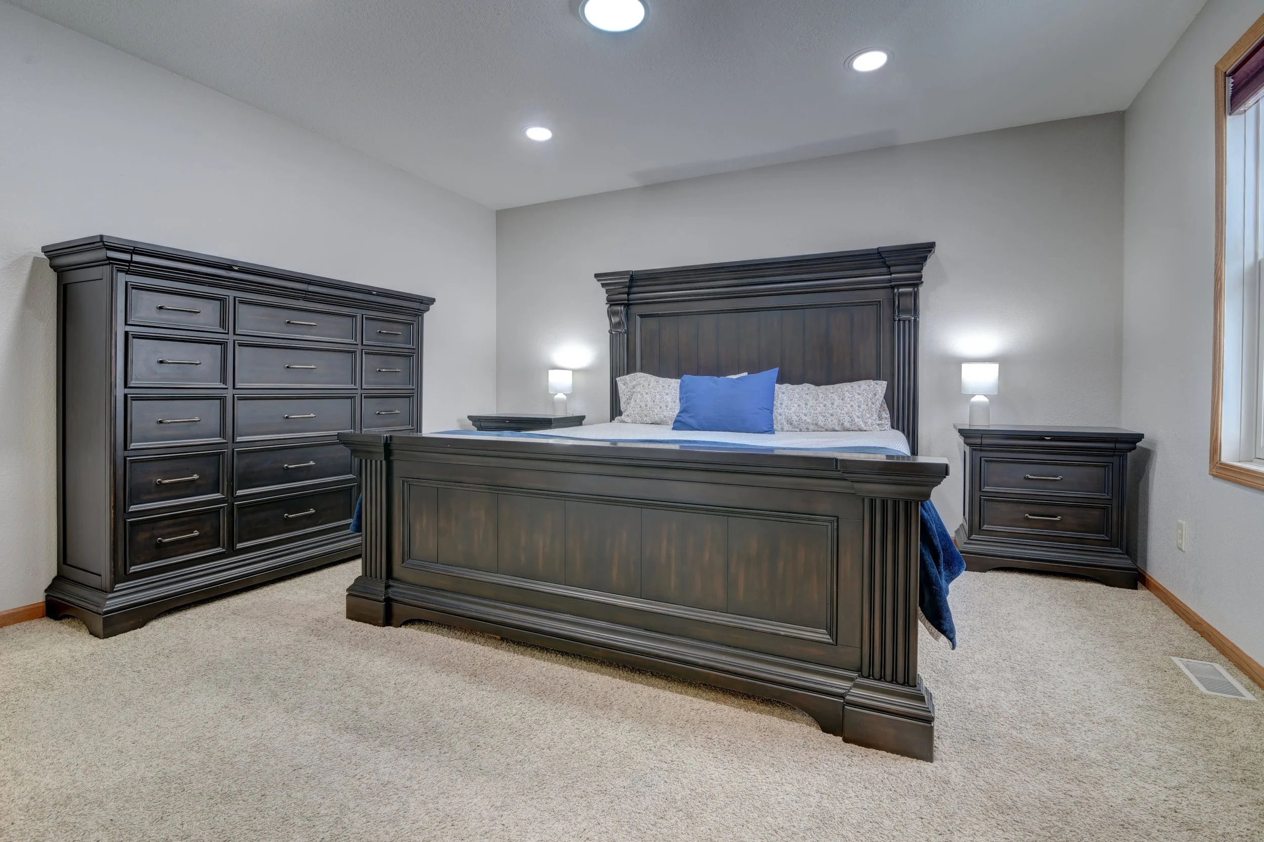 Bedroom with dark wood furniture including a bed, a dresser, and two nightstands, with white walls and a beige carpet.