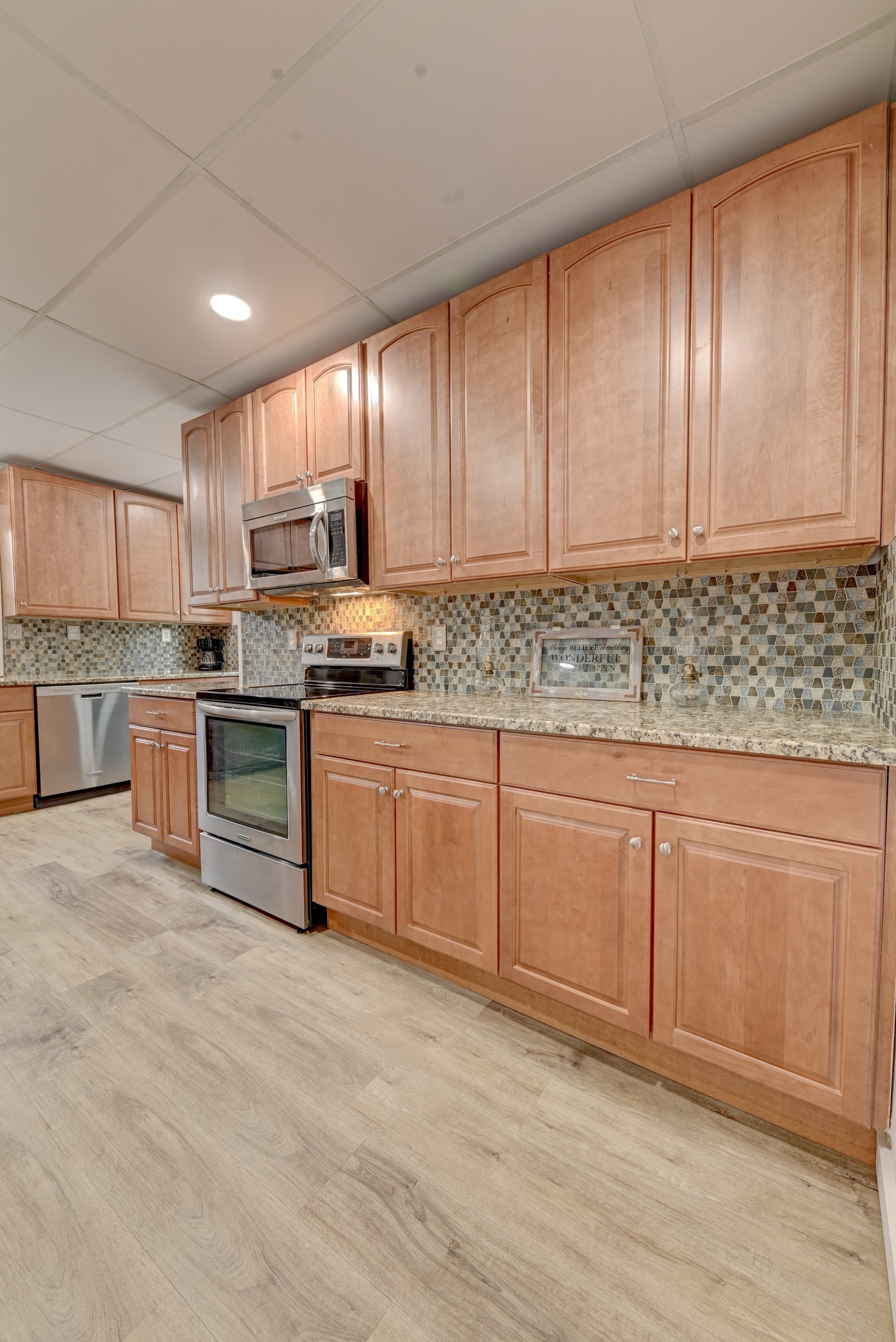 Kitchen with wooden cabinets, stainless steel microwave and stove, mosaic tile backsplash, granite countertops, and light wood flooring.