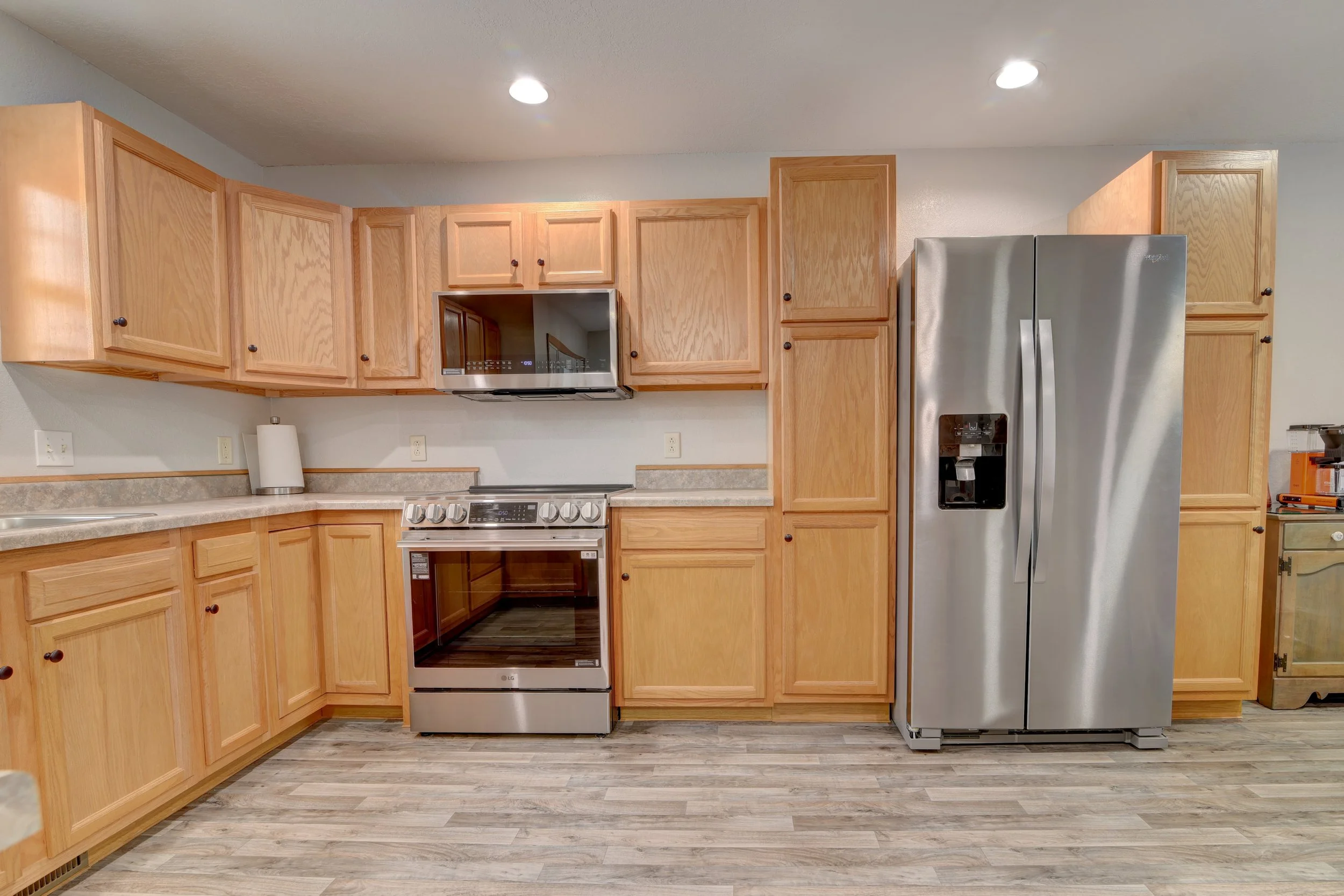 Kitchen with wooden cabinets, stainless steel refrigerator, oven, microwave, countertop, and wooden floor.