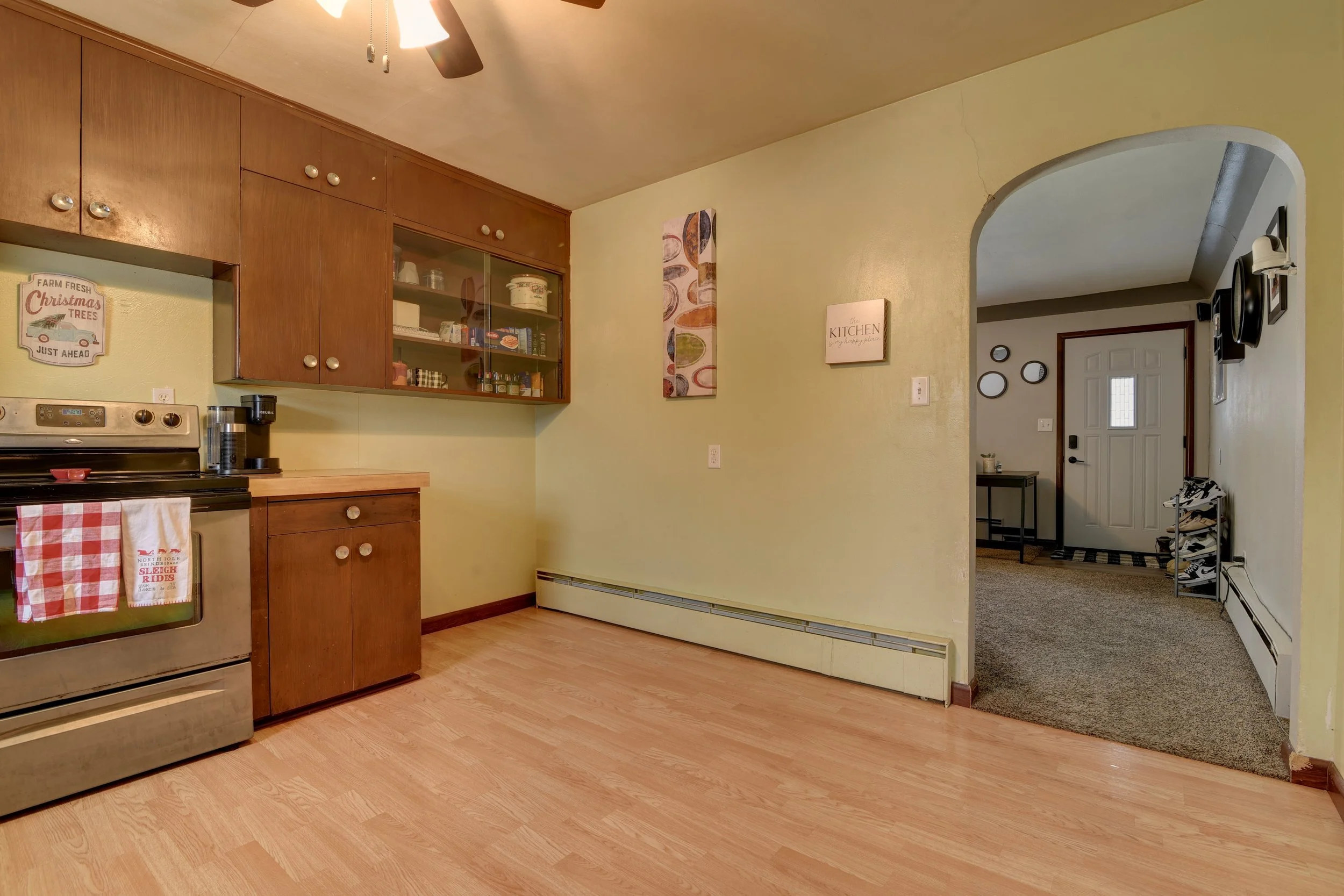 Empty kitchen with wooden cabinets and yellow walls, opening to an entryway with a shoe rack and front door.