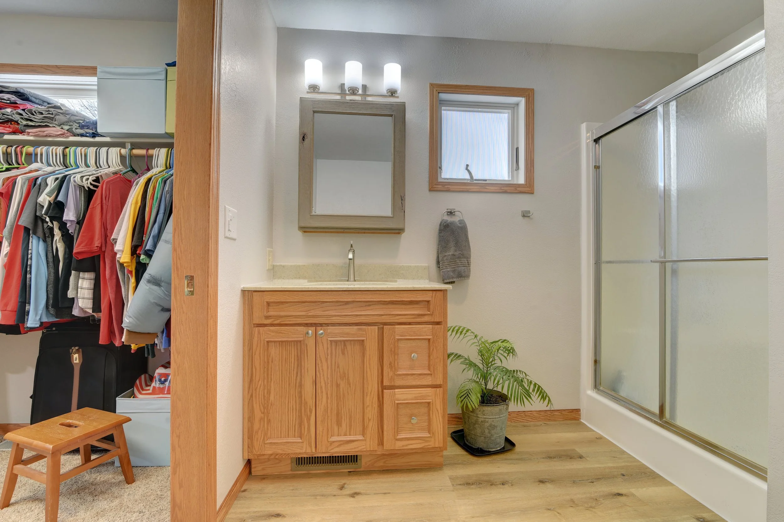 Bathroom with wooden cabinet, mirror, small window, towel holder, potted plant, and shower enclosure.