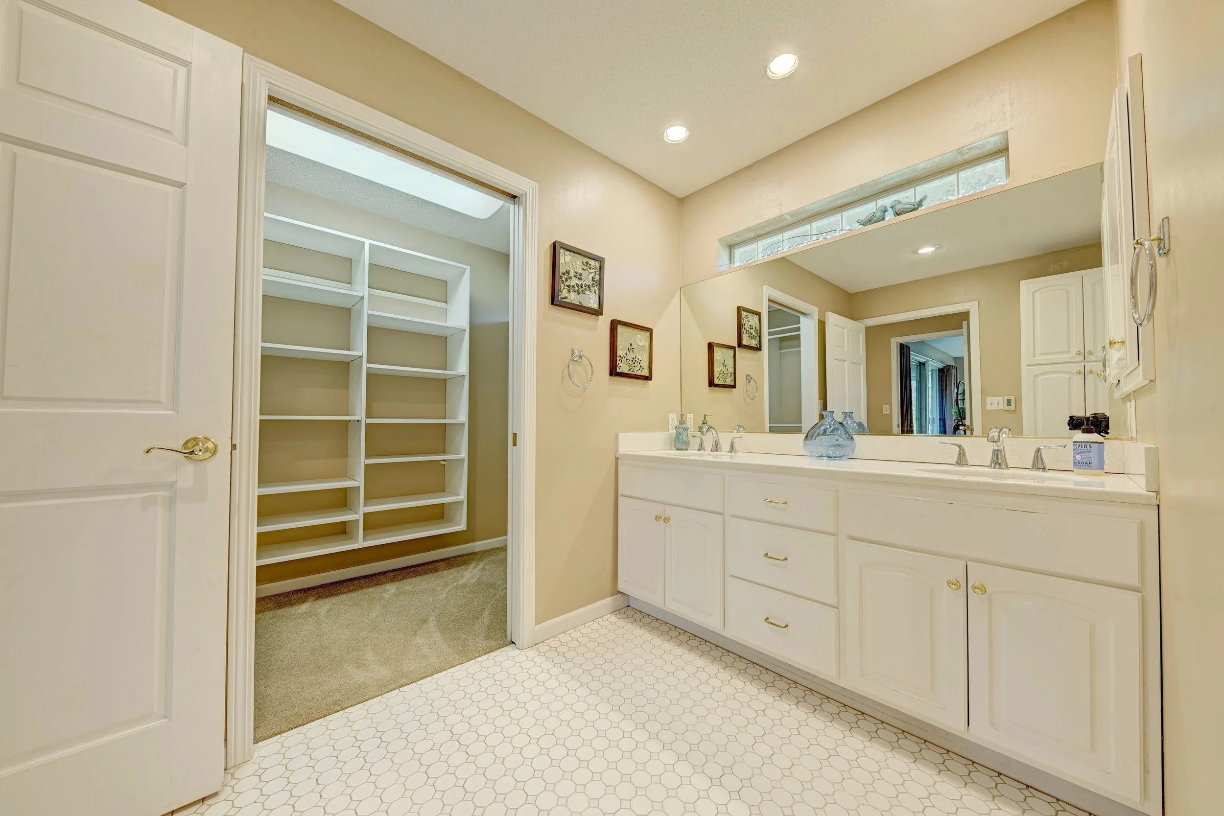 Bathroom with white vanity, large mirror, decorative framed artwork, storage cabinets, and a laundry area with shelving.