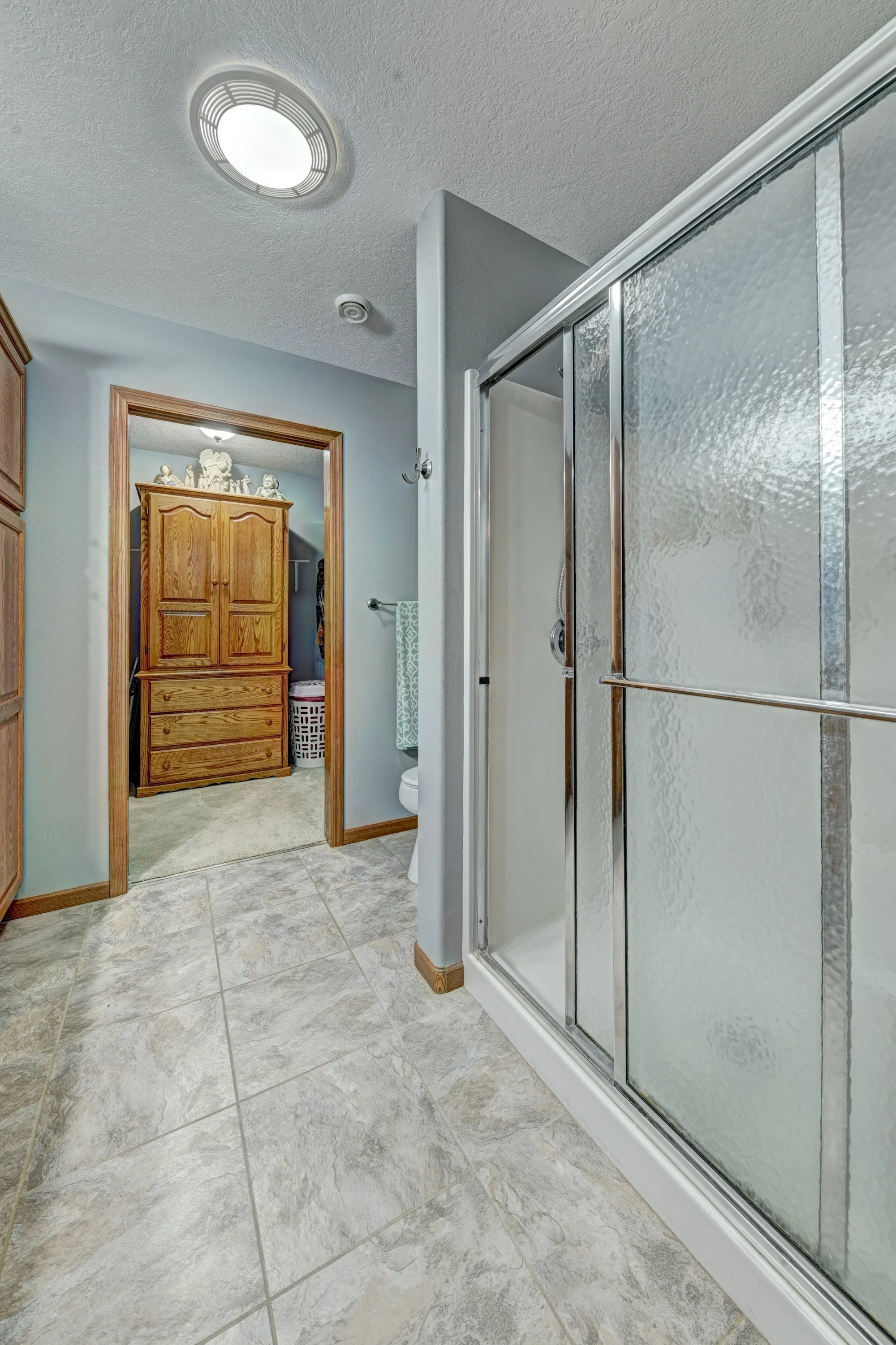 Bathroom with shower enclosure, wooden cabinet, and tiled floor.