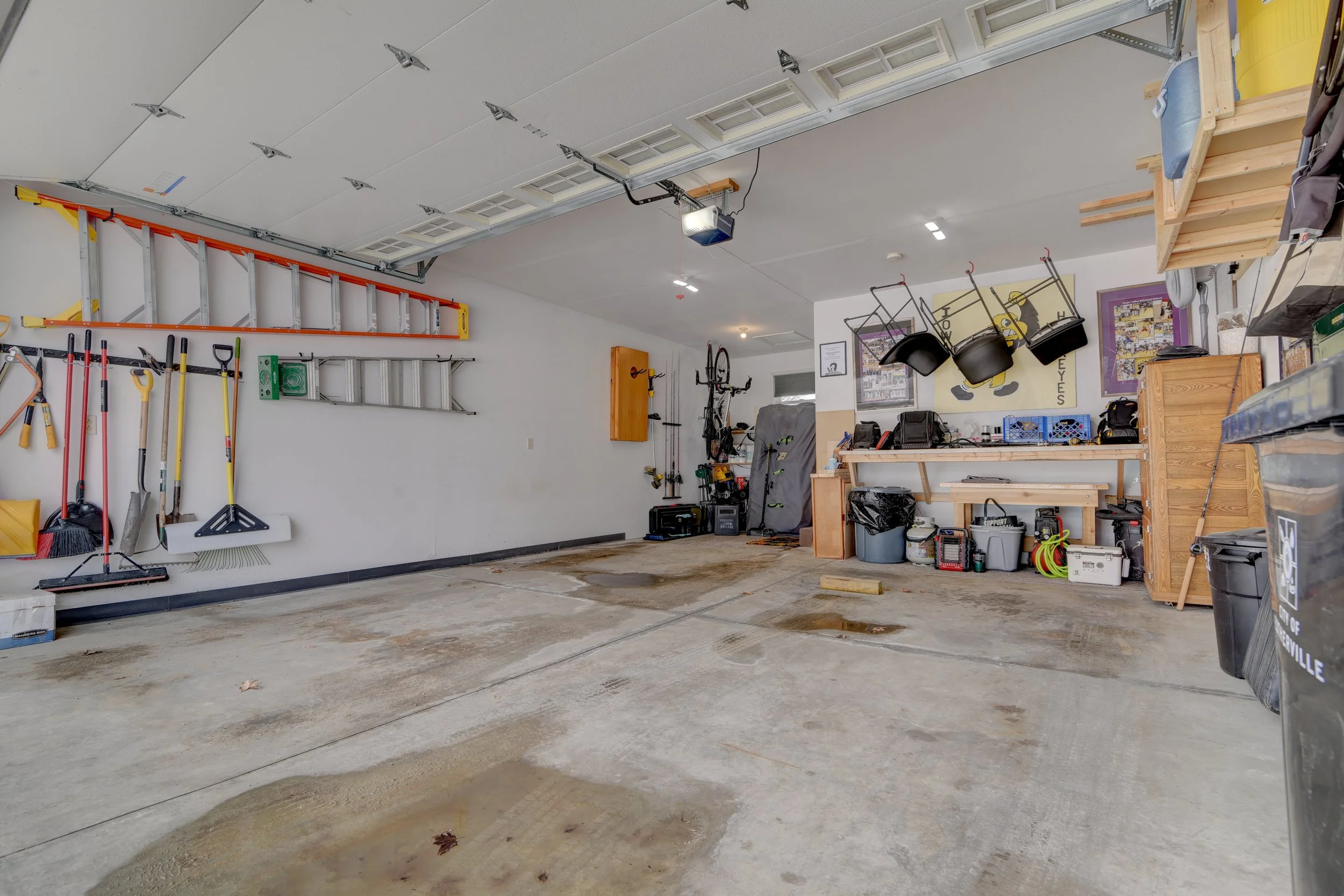 Organized garage with tools on wall, including shovels, brooms, and working equipment, with a workbench and storage boxes.