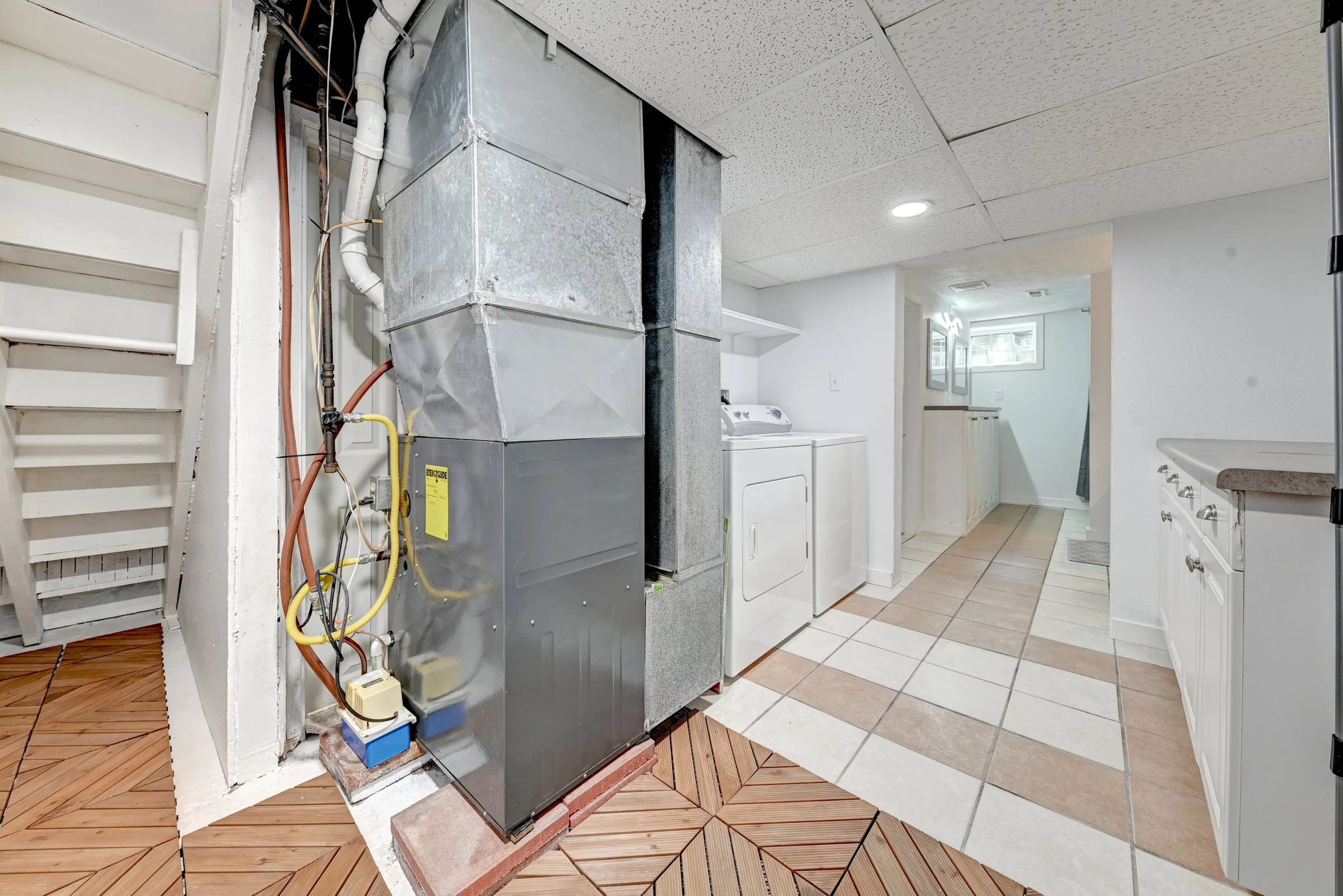 HVAC system in a basement with laundry area visible in the background, including a washing machine and dryer, in a basement with tiled floors and a ceiling with recessed lighting.