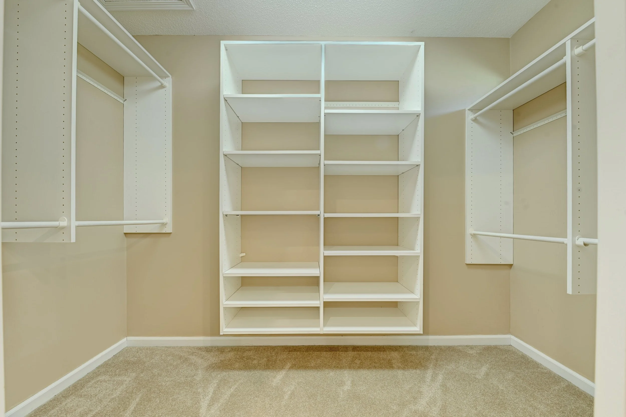 Empty walk-in closet with white shelving units and beige walls.