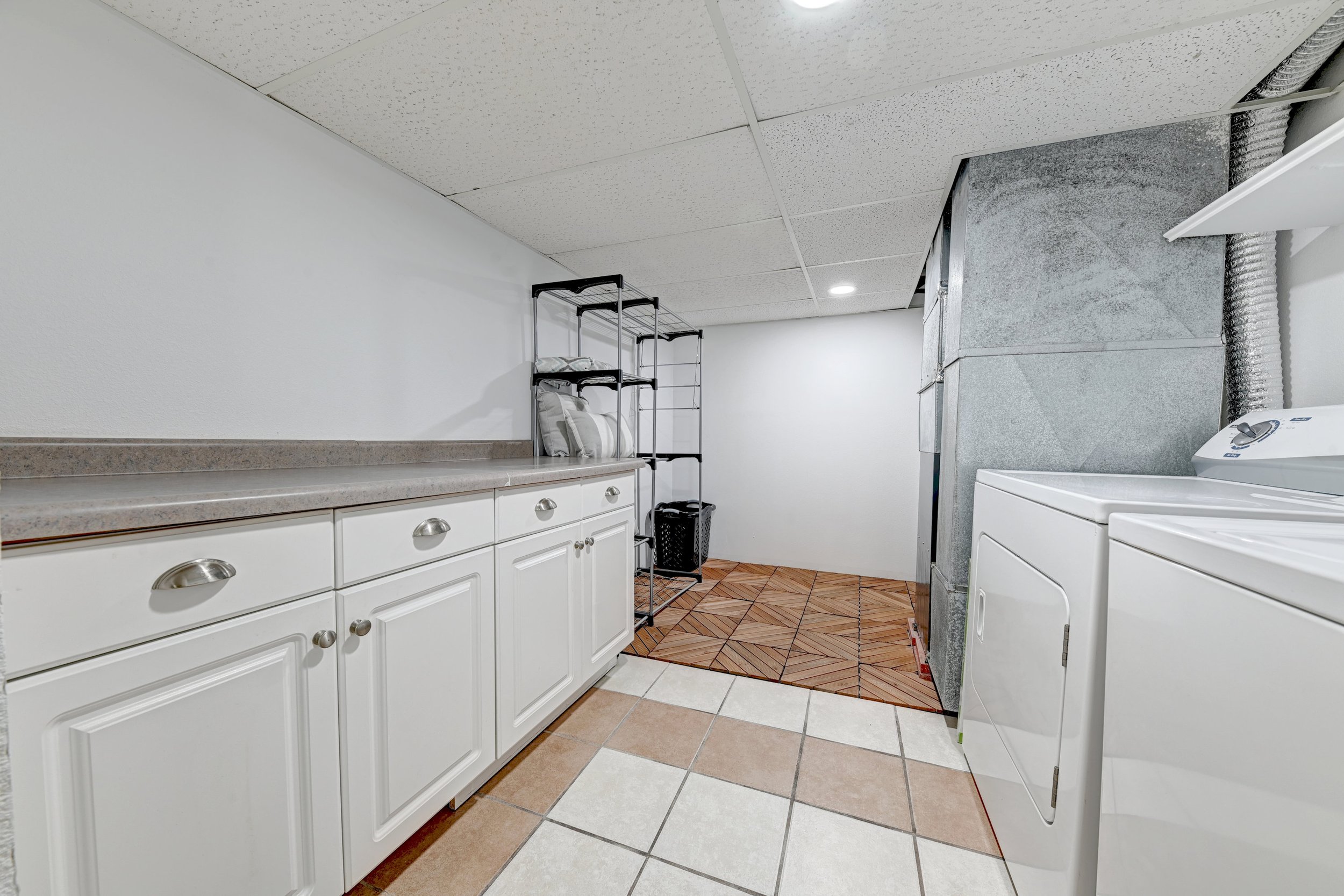 Laundry room with white cabinets, a countertop, a drying rack with pillows, a washing machine, and tiled flooring.