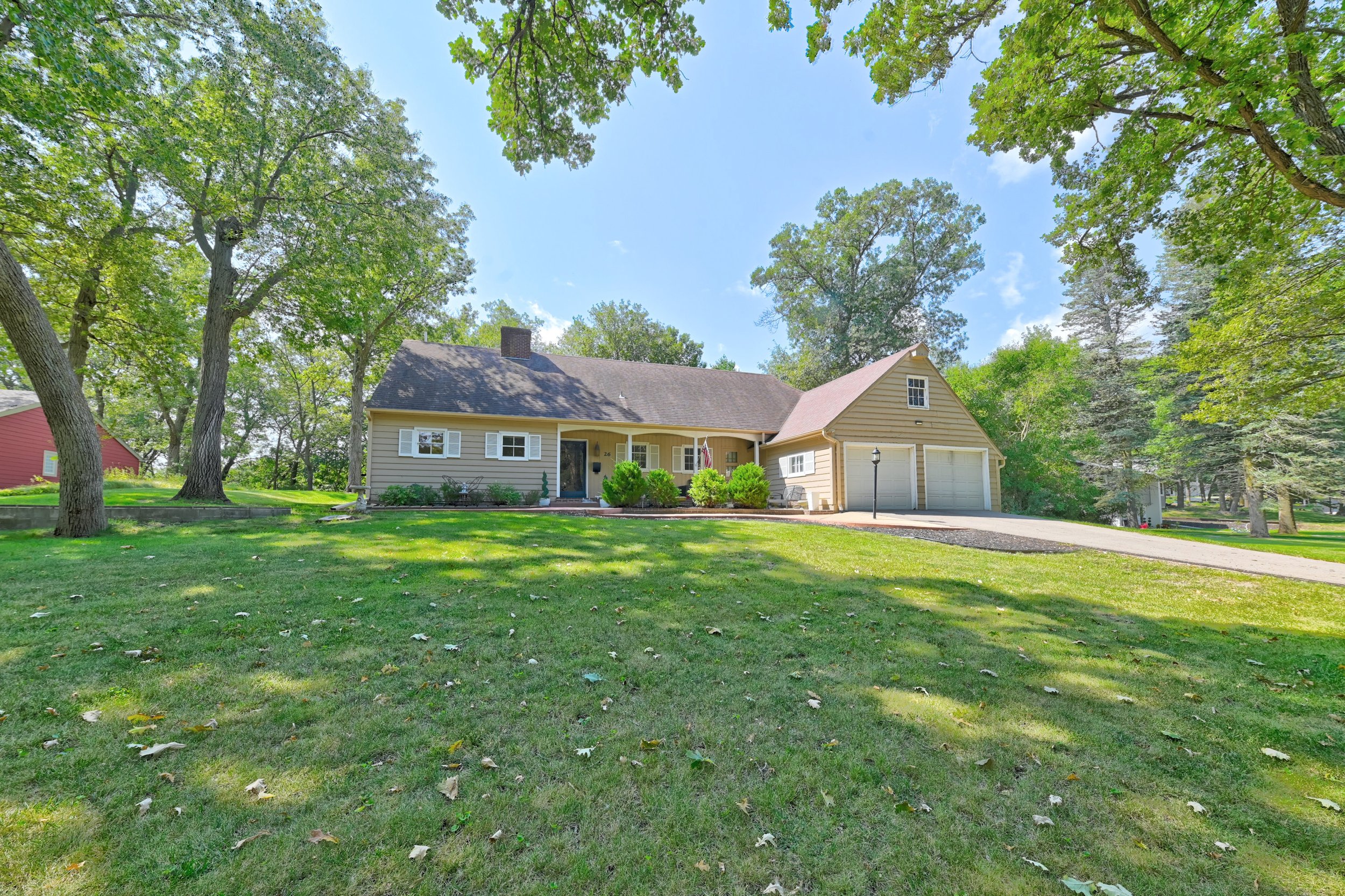 An acreage located in the town of Estherville, Iowa.  A house with a yellow exterior, white shutters, and a brown roof, surrounded by trees and a well-maintained lawn under a partly cloudy sky.