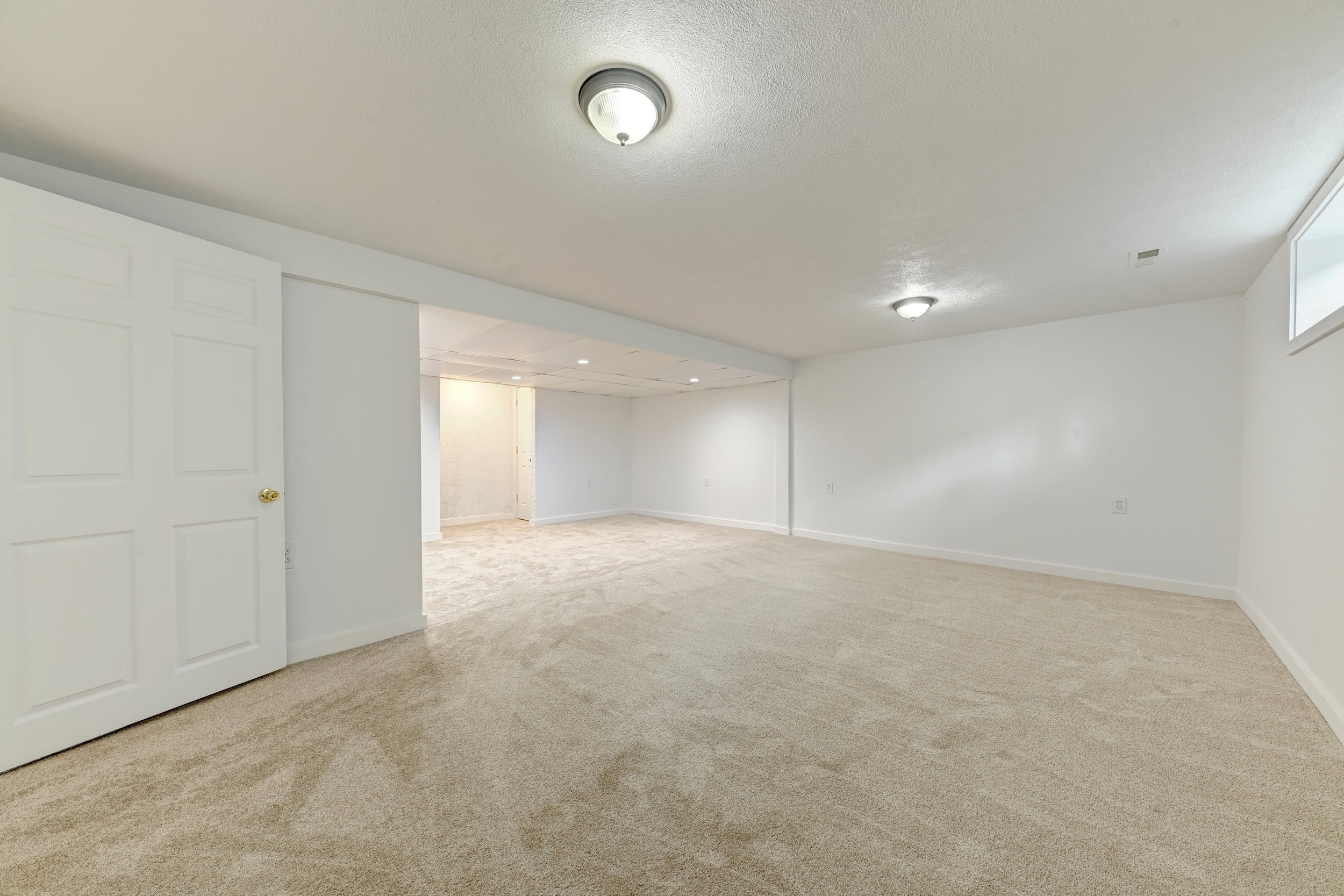 Empty room with white walls, beige carpet, and a ceiling light fixture.