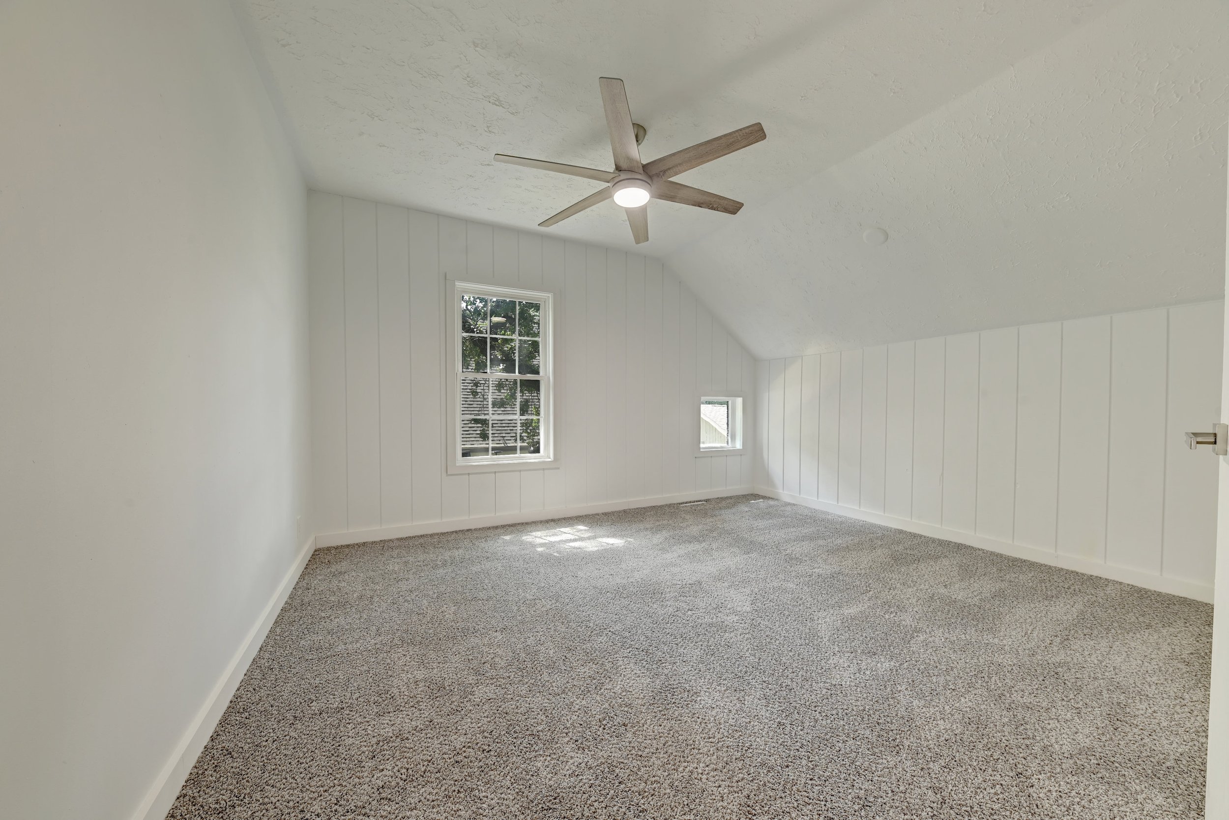 Empty room with white walls, a sloped ceiling, two windows, carpeted floor, and ceiling fan.